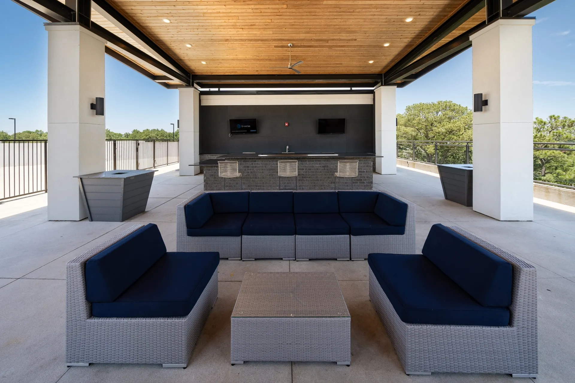 Modern outdoor lounge area with sleek wicker furniture and a stylish bar under a wood-paneled ceiling, perfect for relaxation and social gatherings.