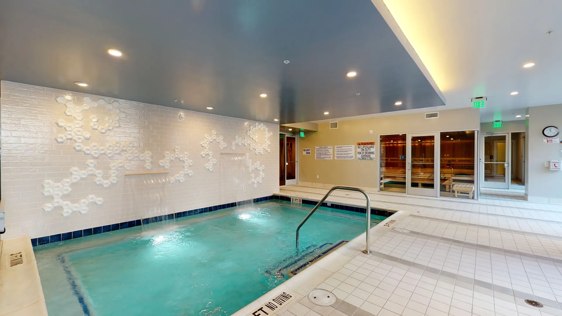 Luxurious indoor pool area with a stylish waterfall feature and adjacent sauna, offering a relaxing retreat.