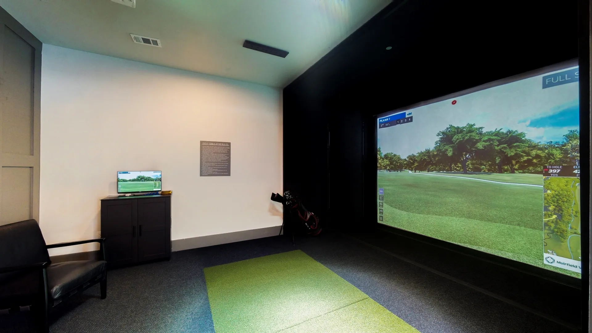 Modern indoor golf simulator room featuring a professional setup with green putting mat and interactive screen.