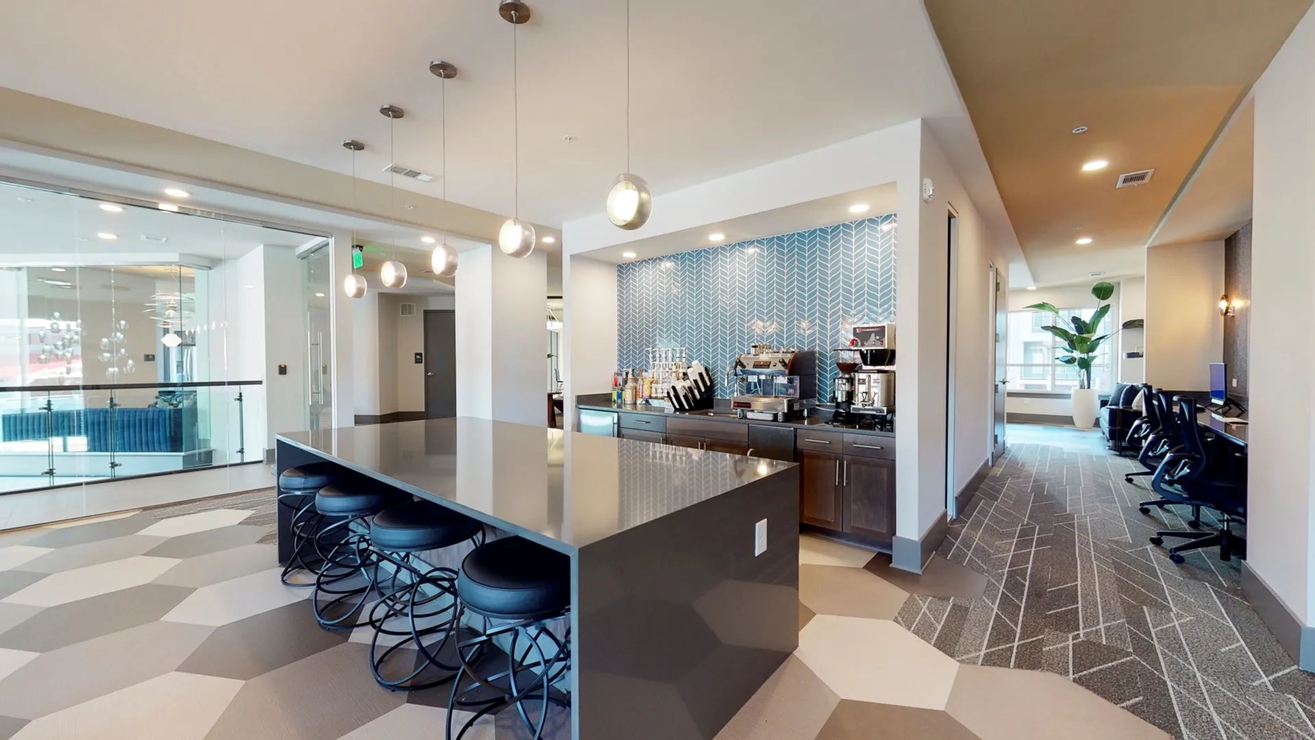 Modern common area with sleek kitchen island, stylish bar stools, and cozy workstations; featuring chic lighting and contemporary decor.