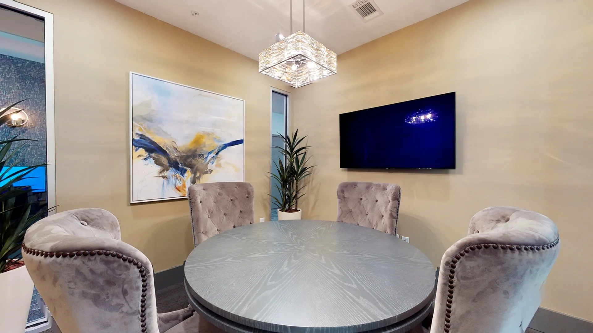 Elegant dining room with a round table and plush chairs, featuring modern art and a sleek TV on the wall.