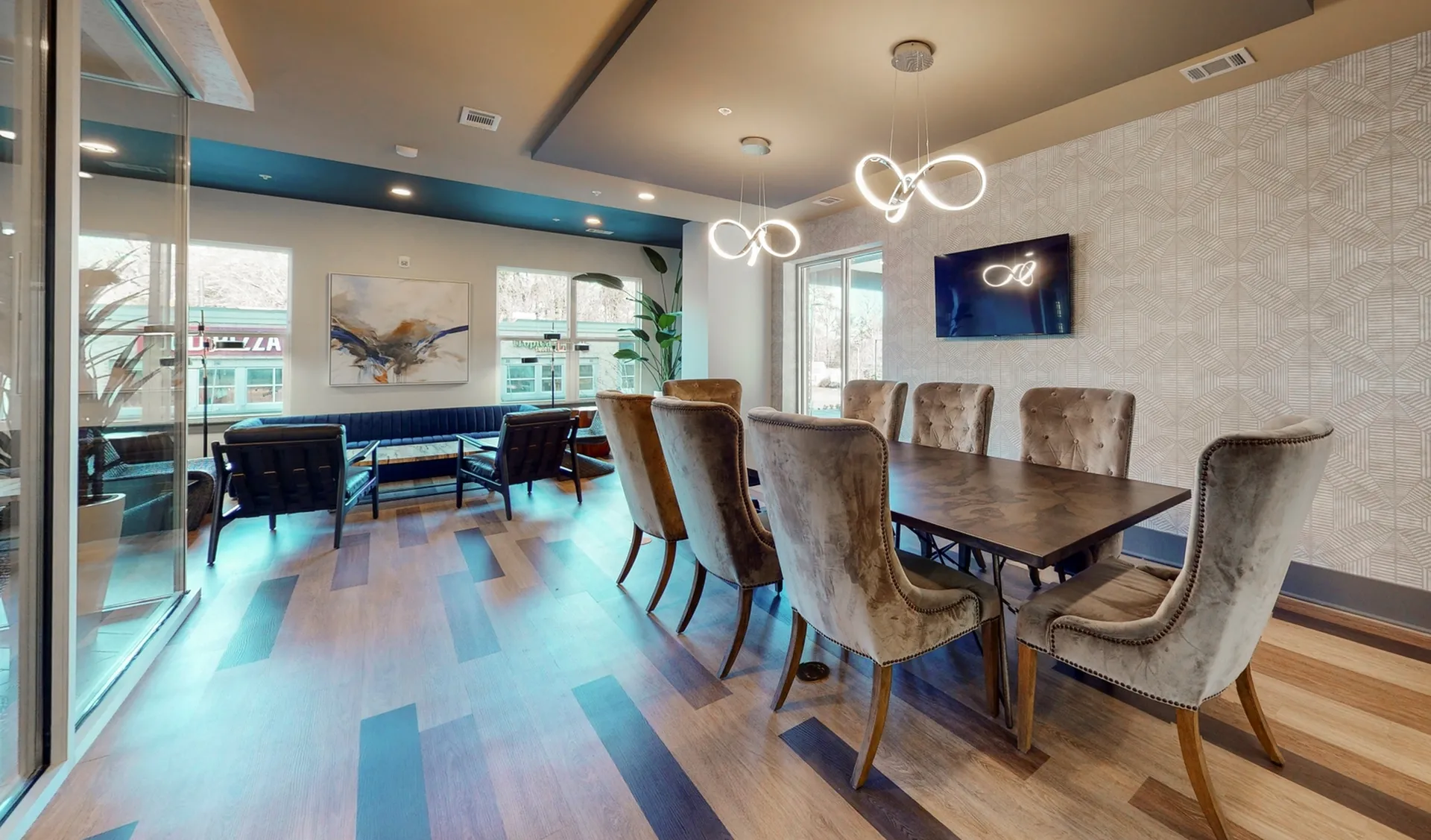 Elegant communal space featuring chic velvet chairs, modern lighting fixtures, and a sleek wooden table, perfect for meetings or gatherings.