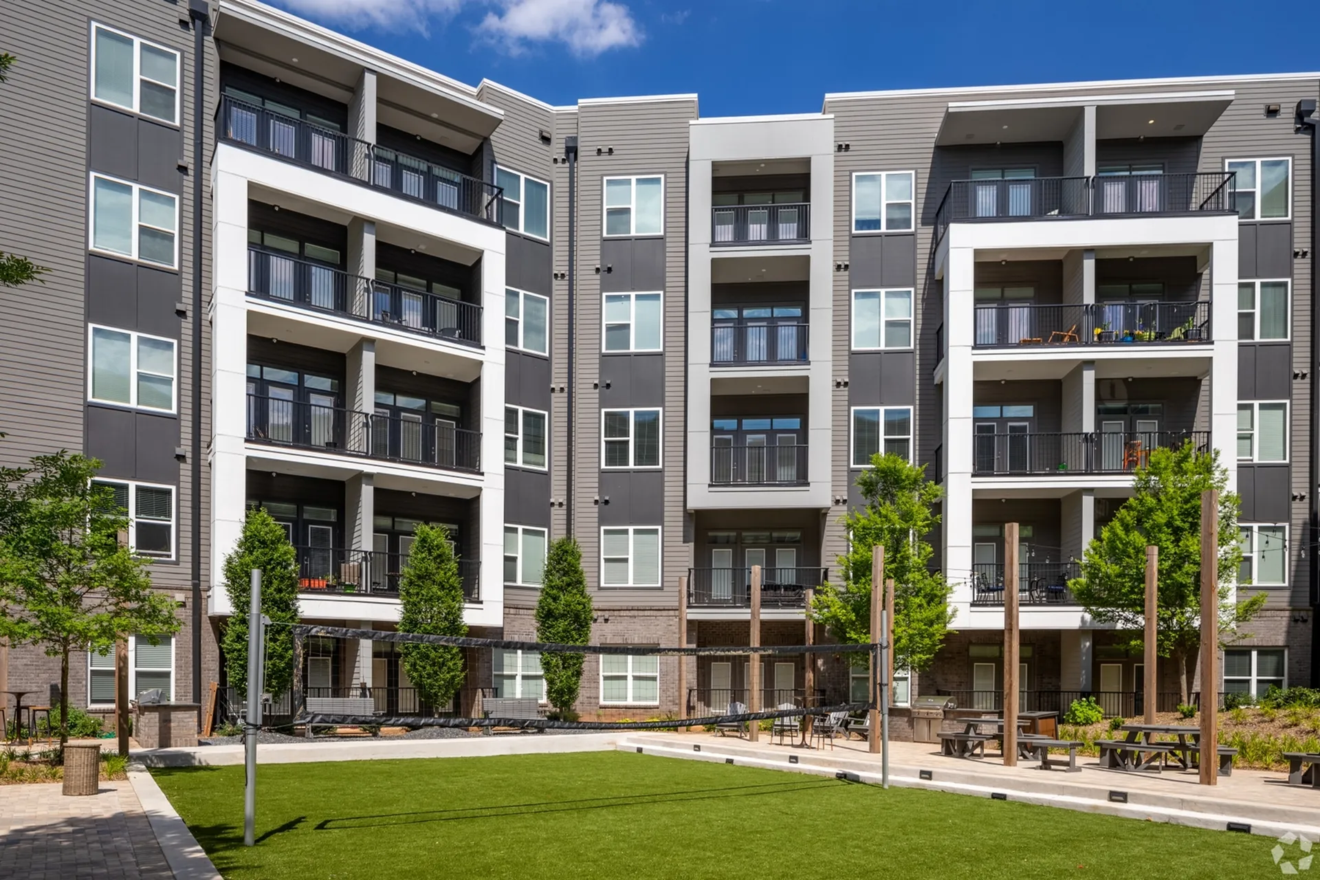 Modern apartment complex with spacious balconies and lush green courtyard, perfect for outdoor activities.