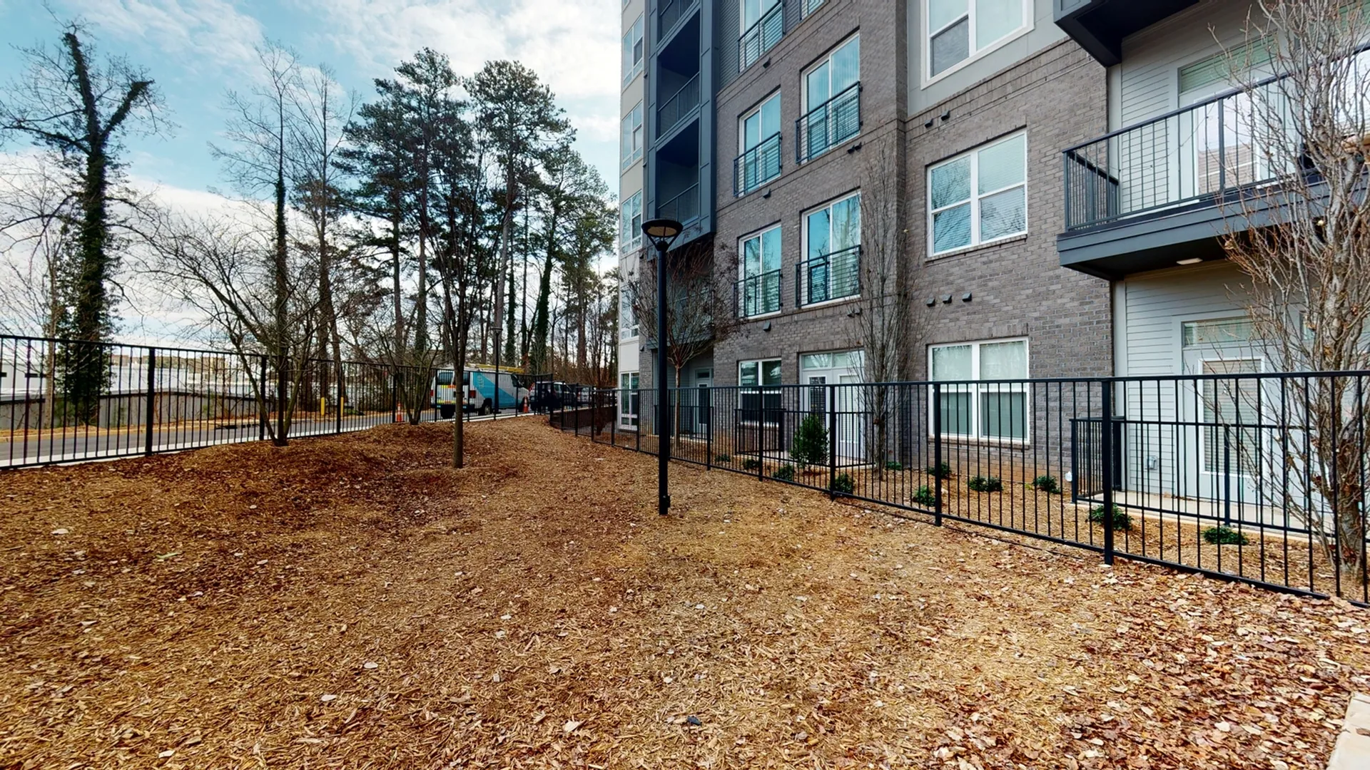 Modern apartment building with sleek balconies and fenced perimeter, set amidst a peaceful wooded area.