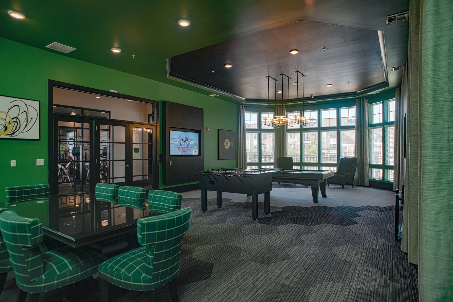 Elegant lounge area with modern green accents, featuring a foosball table, plush seating, and floor-to-ceiling windows for natural light.