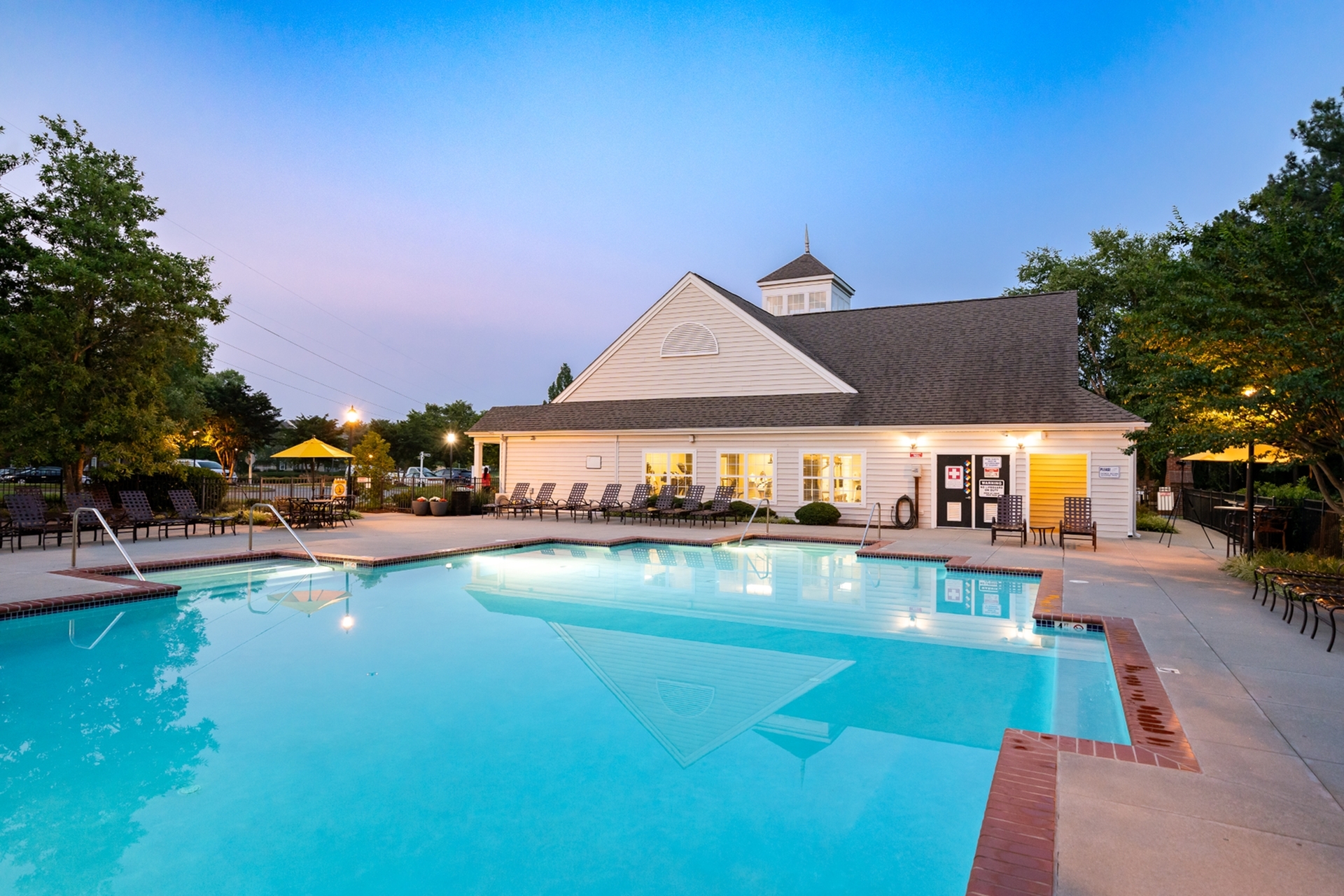 Inviting outdoor pool area with elegant lounge chairs and charming clubhouse at sunset, perfect for relaxation.