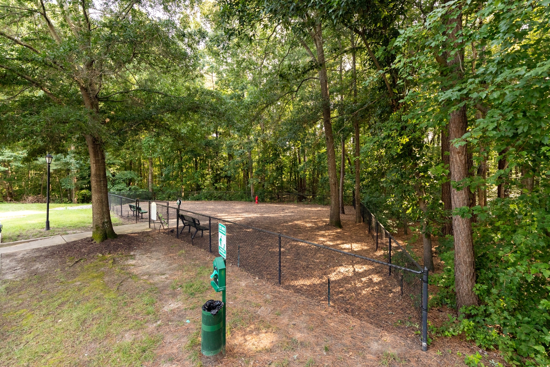 Serene, fenced dog park nestled in a lush, green woodland with convenient seating and a walking path.