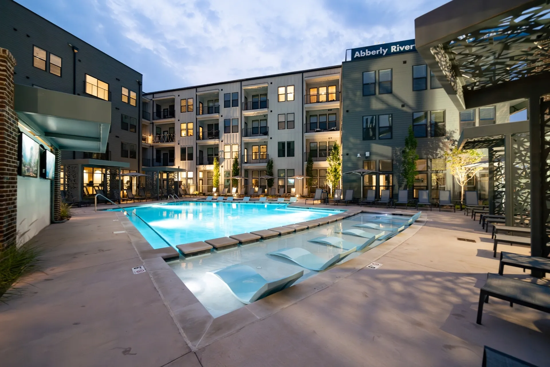 Elegant apartment complex with illuminated pool and modern lounge areas, offering a luxurious outdoor living experience.