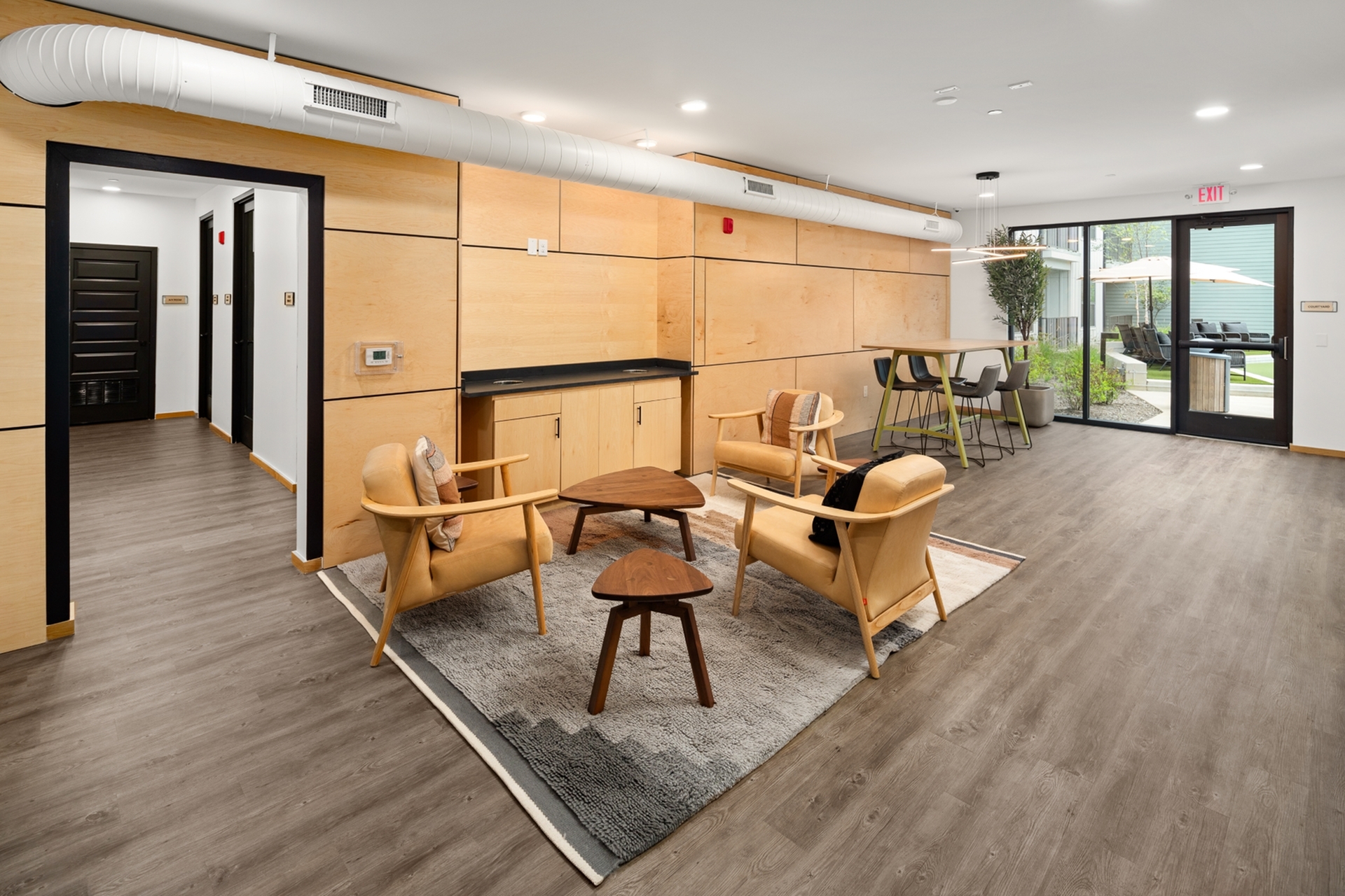 Modern living space with sleek wooden paneling, cozy seating area, and floor-to-ceiling windows overlooking a lush garden patio.