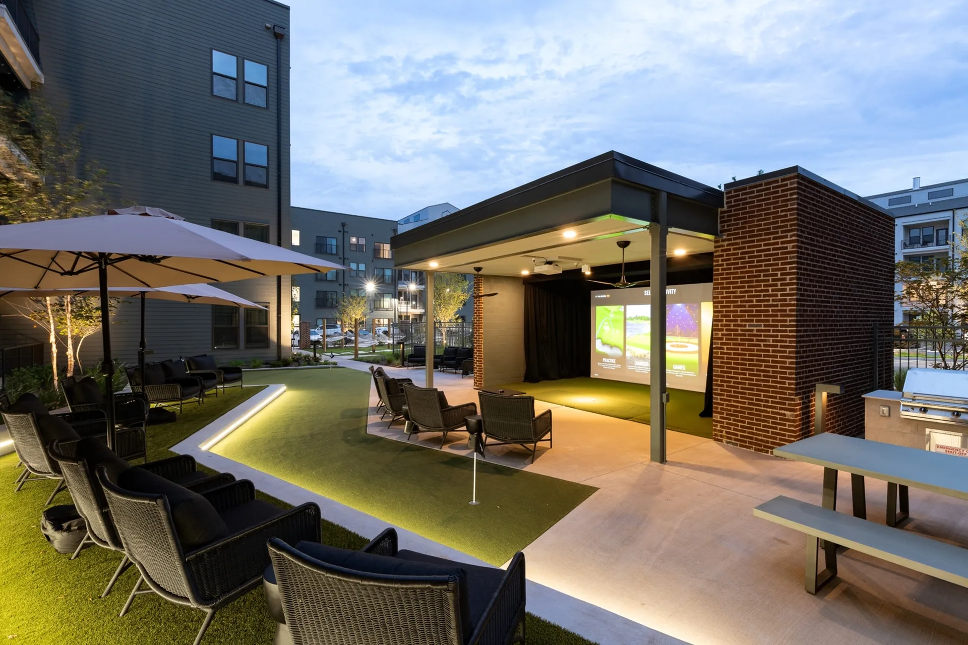 Luxurious outdoor lounge area with modern seating, a large screen for entertainment, and ambient lighting under a stylish canopy.
