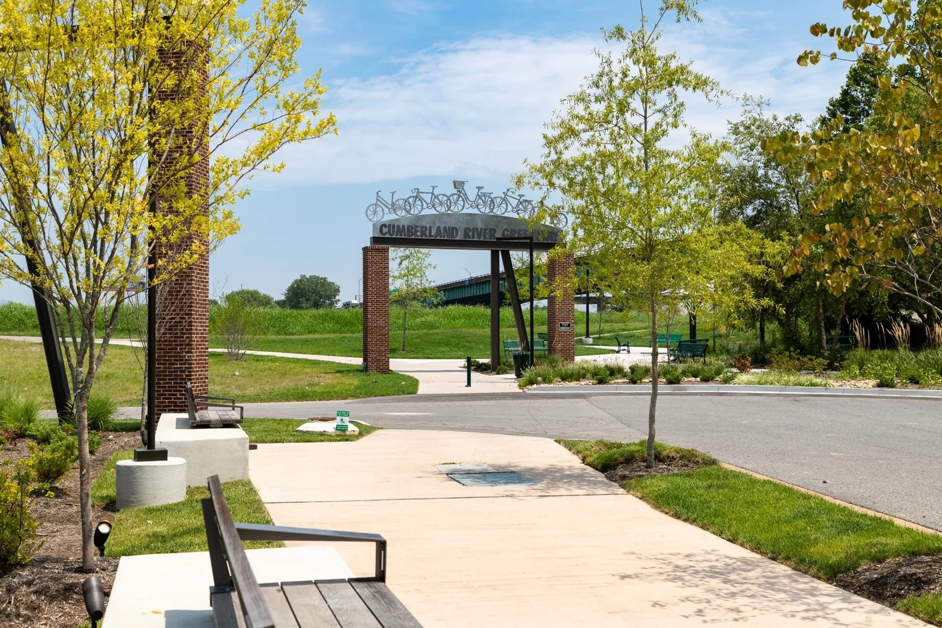 Inviting pathway leading to a lush park entrance with charming bicycle-themed metalwork and scenic greenery.