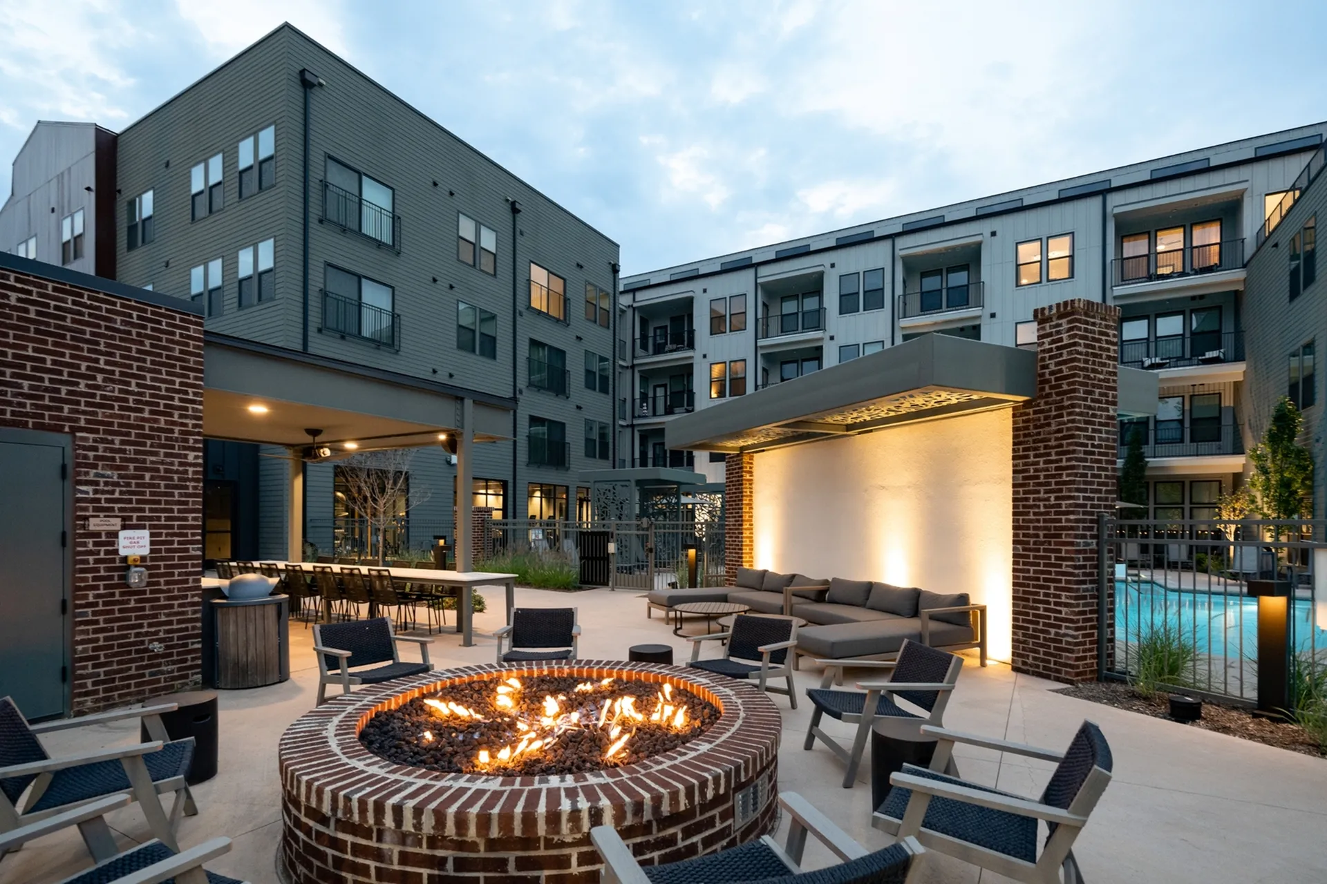 Modern apartment complex courtyard featuring a cozy fire pit, stylish seating area, and evening lighting.