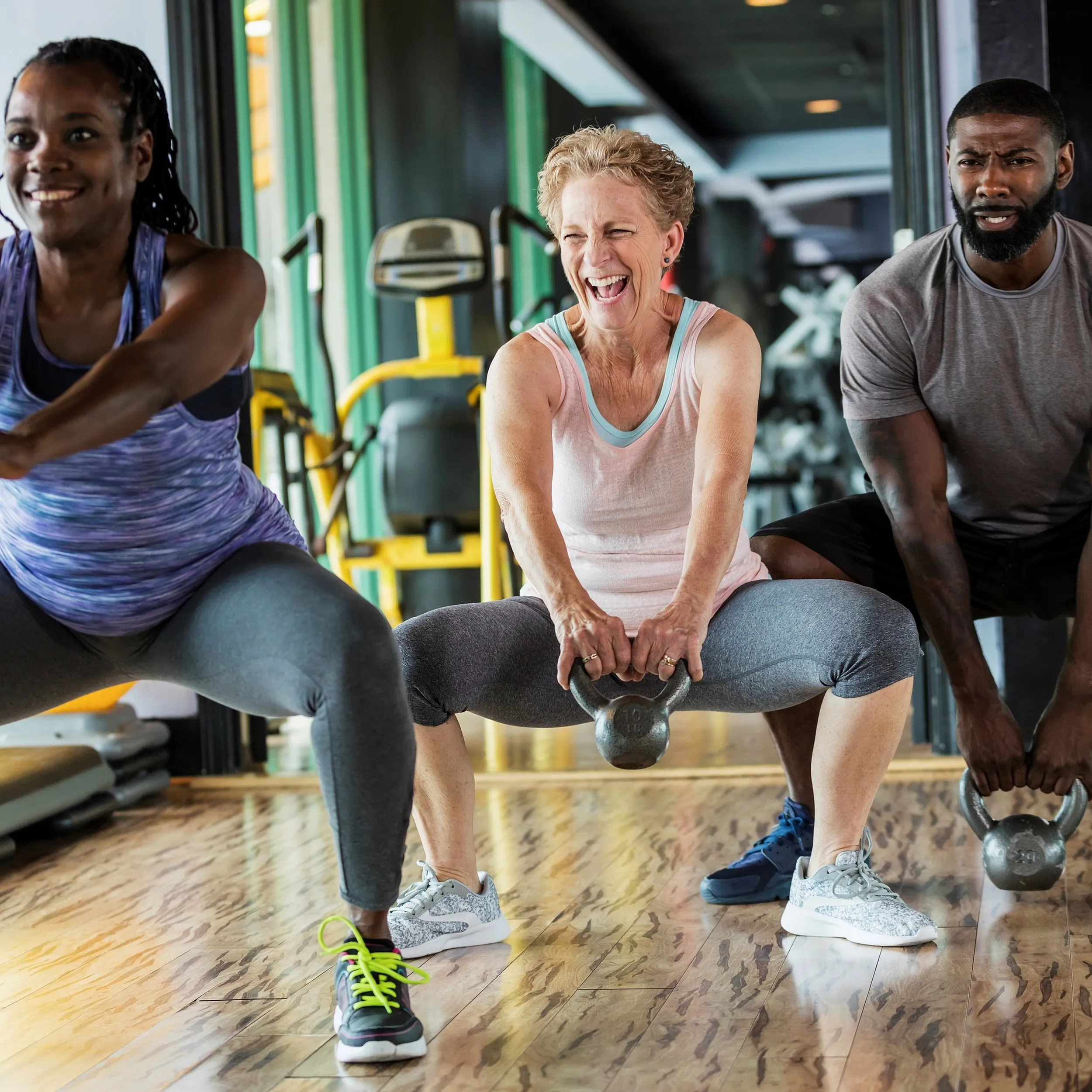 Energetic group workout session with diverse individuals exercising with kettlebells on a sleek wooden floor.