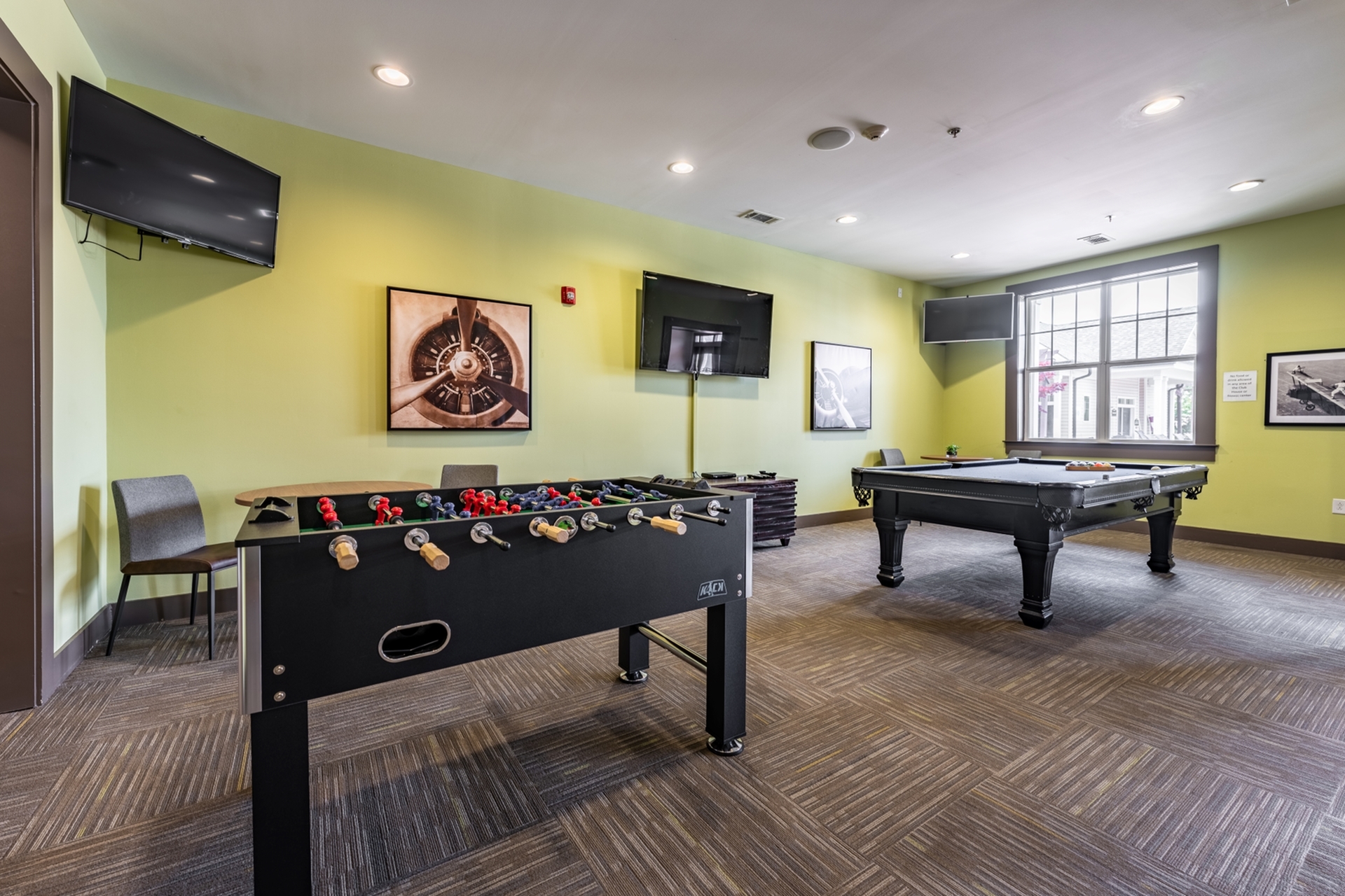 Stylish game room with foosball and billiard tables, vibrant green walls, and modern lighting, perfect for entertainment.