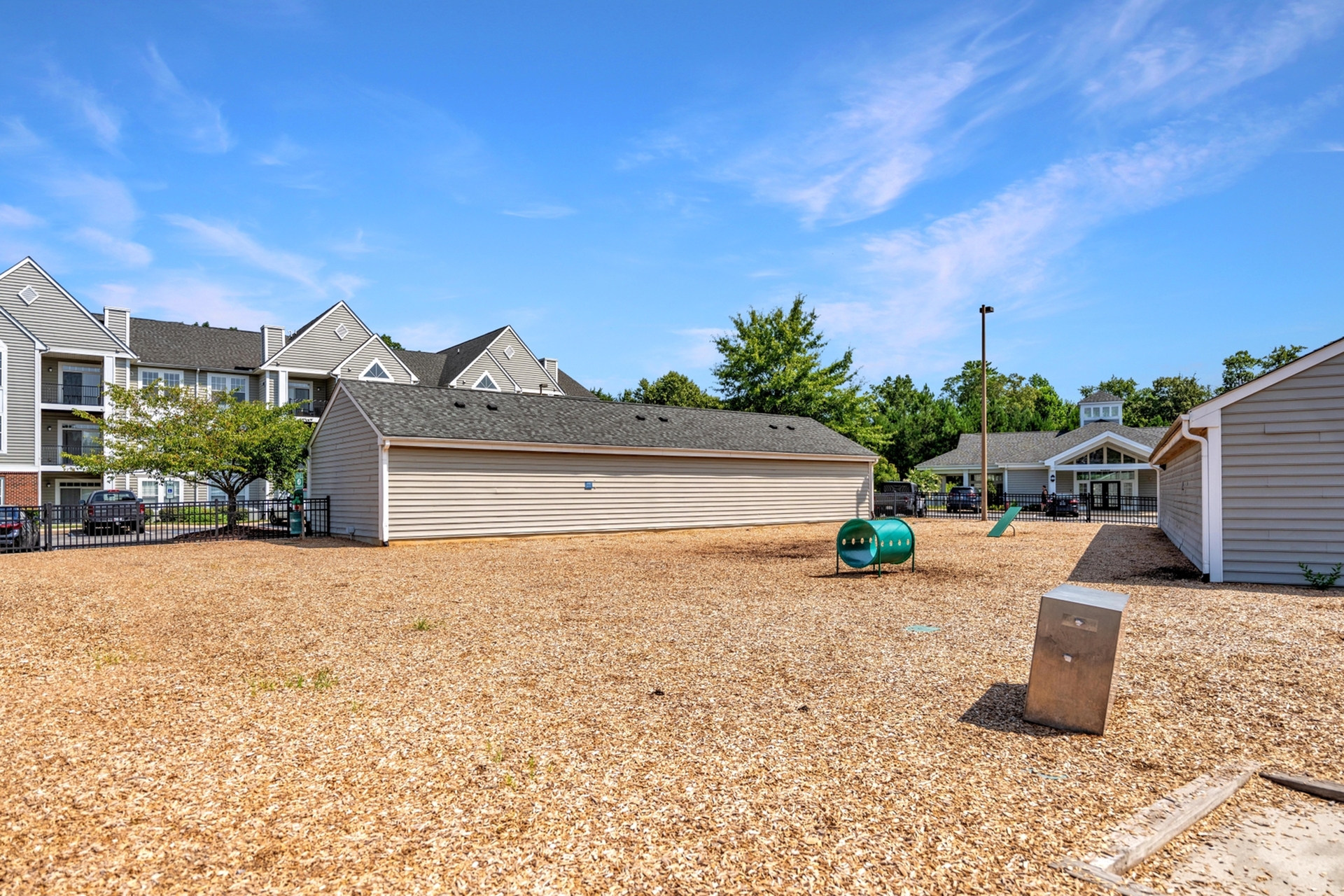 Inviting community playground with mulch area, surrounded by modern apartments and lush greenery, under a vibrant blue sky.