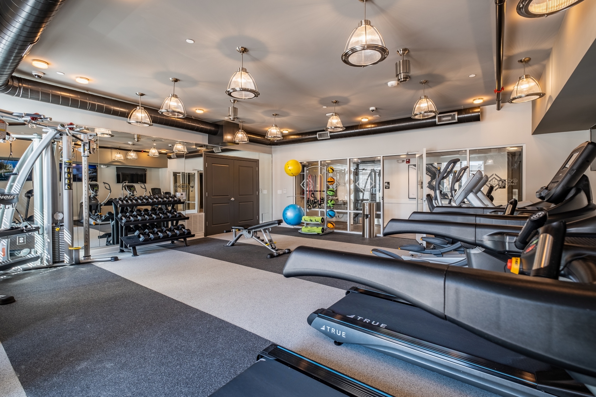 Modern and spacious gym with state-of-the-art treadmills, weight racks, and fitness equipment under stylish pendant lighting.