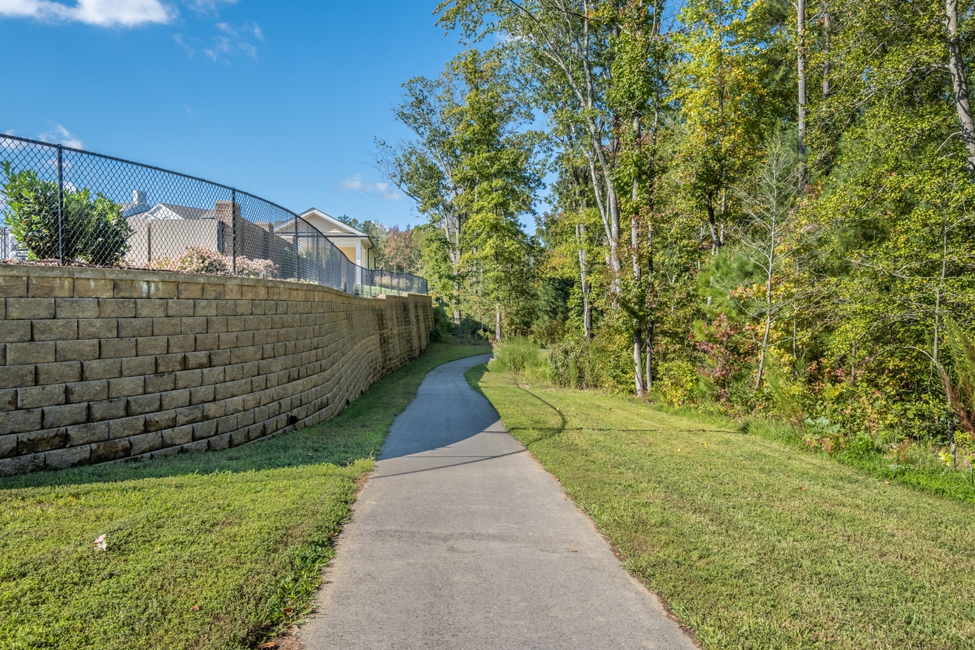 Charming walking path alongside a brick wall with lush trees and vibrant greenery under a clear blue sky.