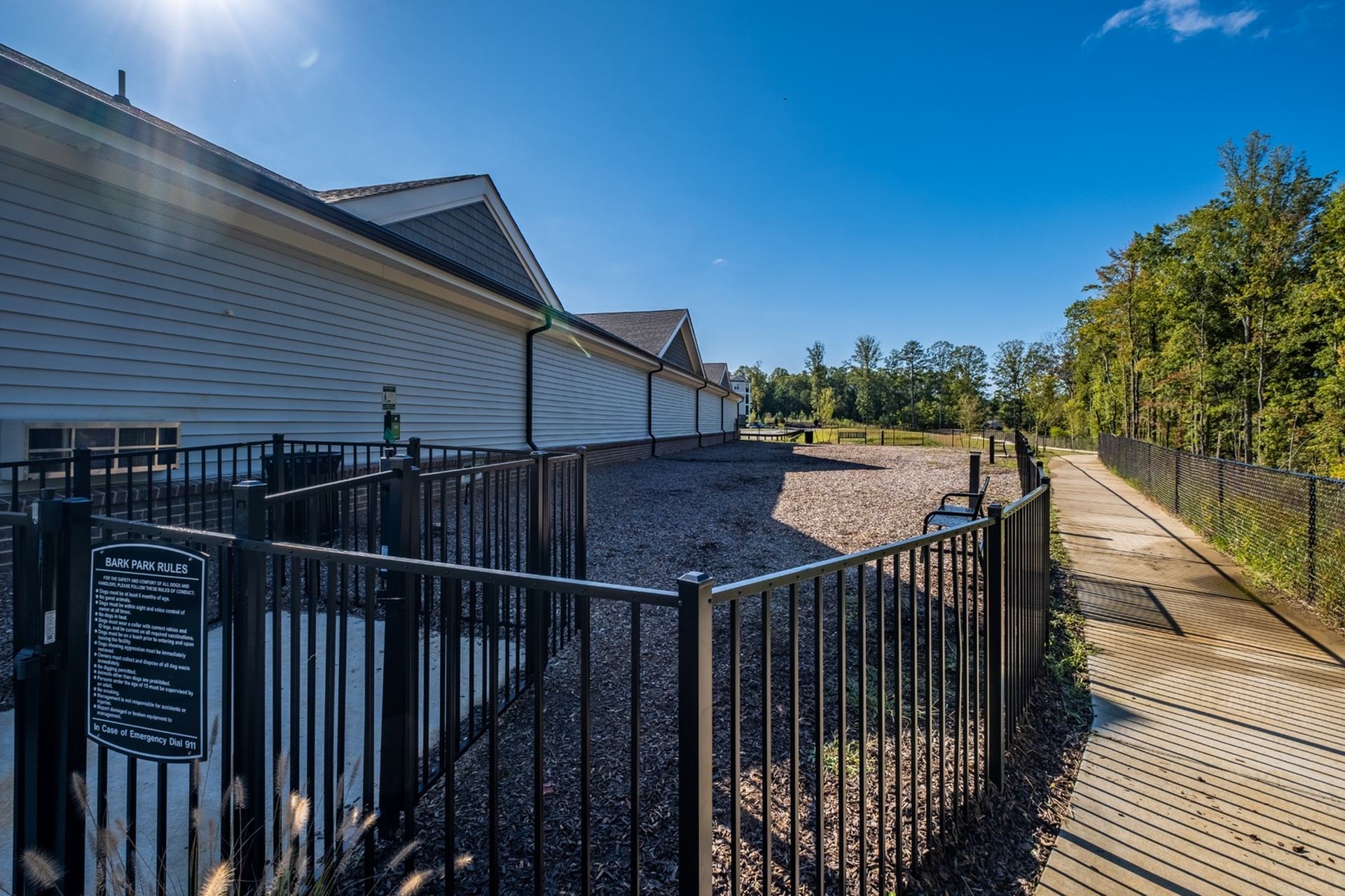 Charming outdoor dog park with secure fencing, bordered by lush greenery and a sunny pathway, perfect for pet-friendly living.