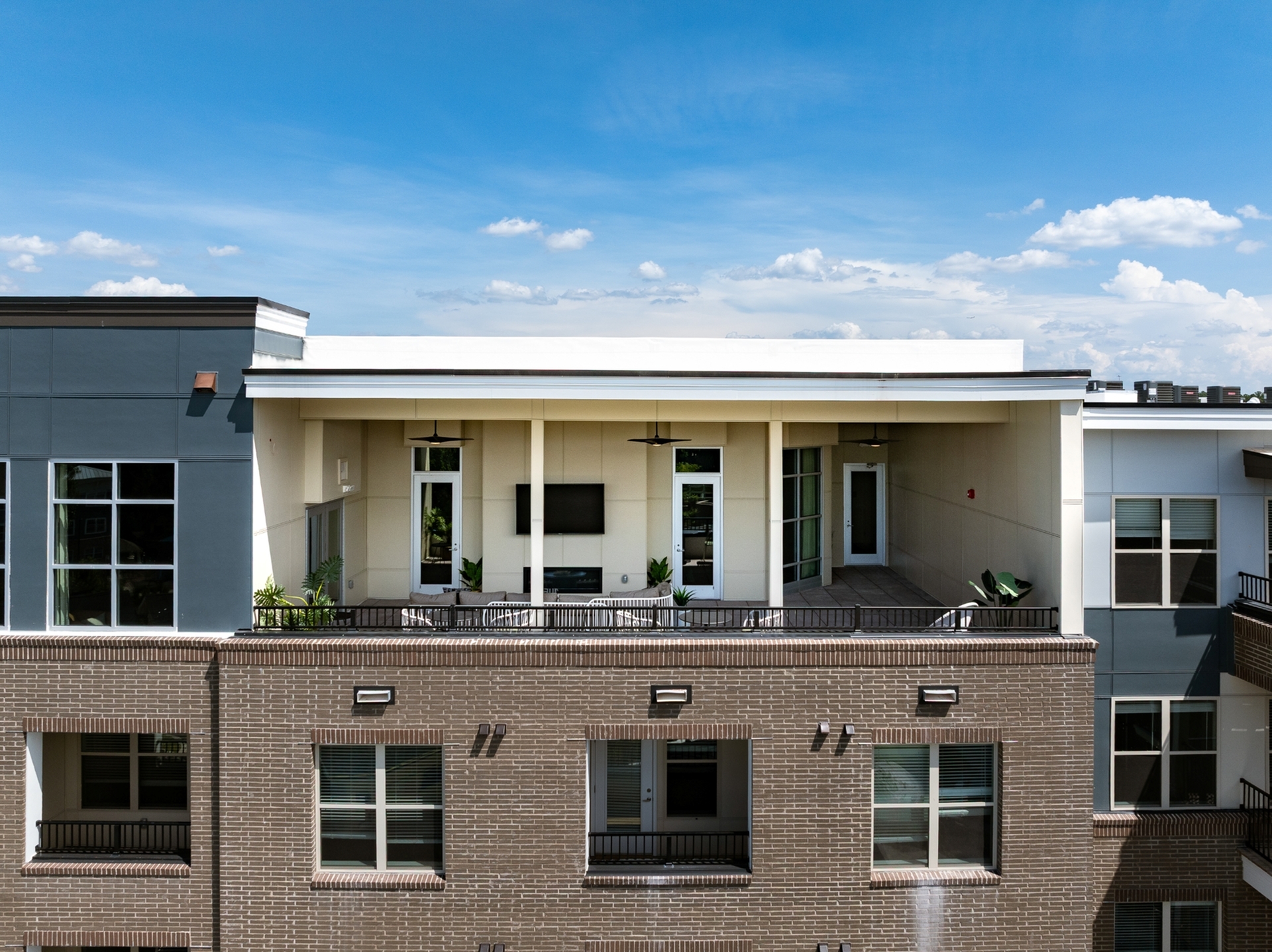 Modern apartment exterior featuring an inviting rooftop patio with seating area, surrounded by lush greenery against a clear blue sky.