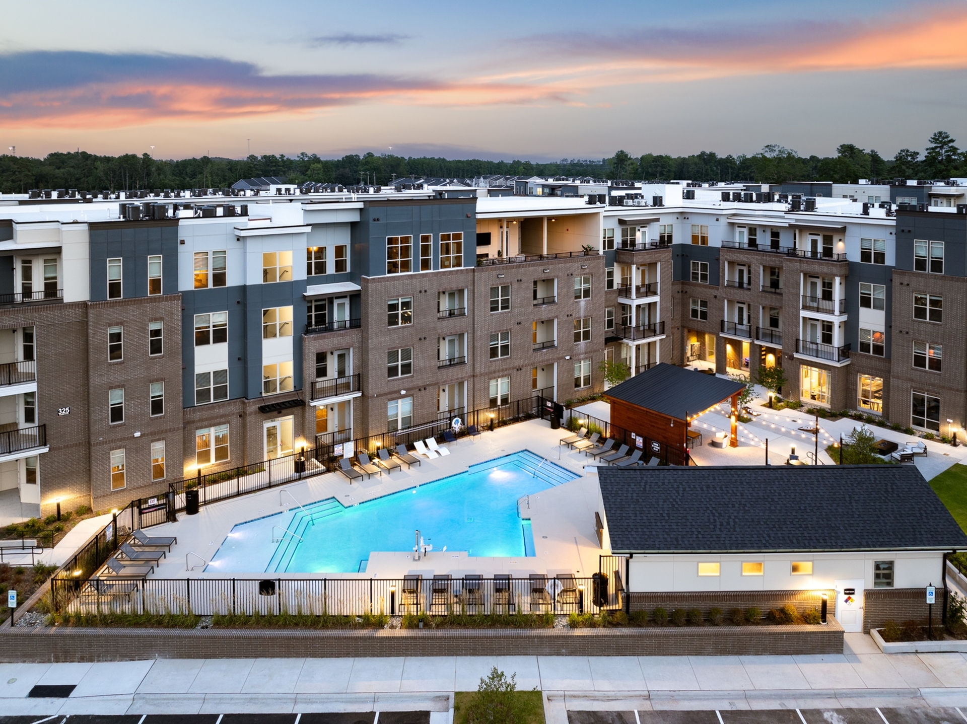Luxury apartment complex at sunset with a sparkling pool, stylish brick façade, and modern amenities, perfect for elegant urban living.