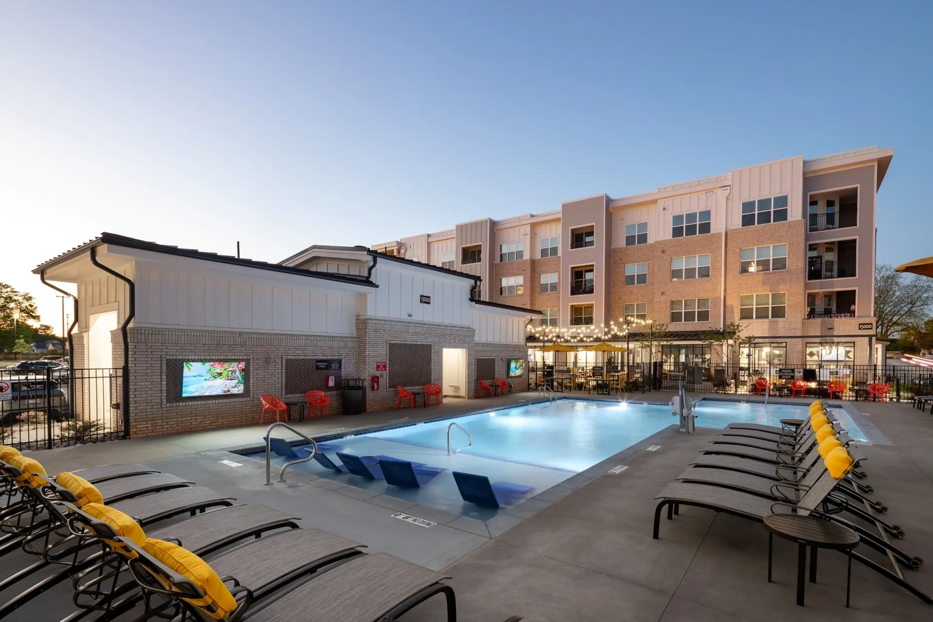 Modern apartment complex with a luxurious illuminated swimming pool, surrounded by stylish lounge chairs and cozy outdoor seating, perfect for relaxation.