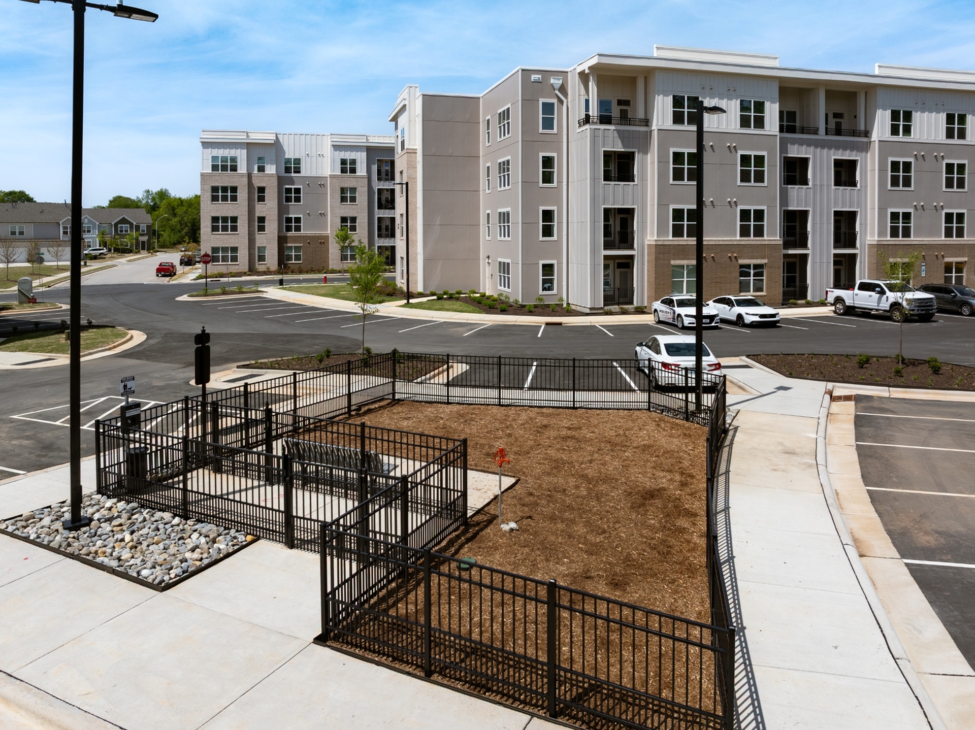 Modern apartment complex with sleek architecture, ample parking, and landscaped grounds on a sunny day.