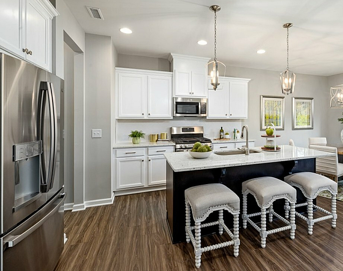 A kitchen with white cabinets, a large island with three stools, and granite countertops at Abberly Alston Townhomes in Cary, NC