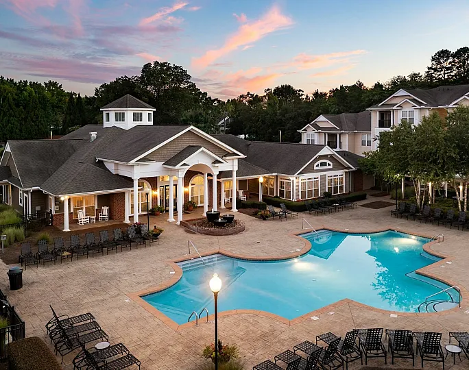 Aerial view of the outdoor pool area at dusk, featuring a resort-style pool with ample lounge seating, and the community clubhouse surrounded by well-maintained landscaping at Abberly Woods Apartments in Charlotte, NCat Abberly Woods Apartm