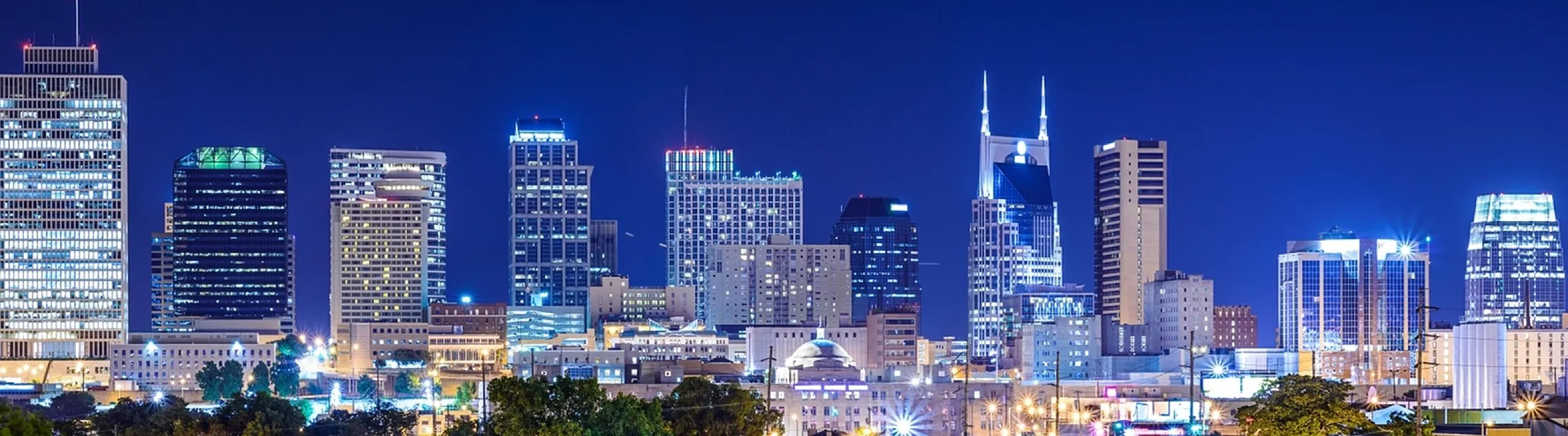 Stunning cityscape view with vibrant lights illuminating modern high-rise buildings against a deep blue night sky.
