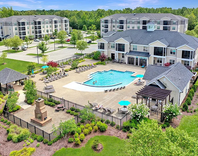 Vibrant apartment community with a sparkling pool, outdoor lounge with fireplace, and lush greenery, offering a serene lifestyle.