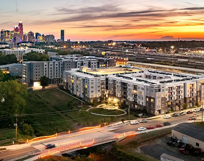 Modern apartment complex situated near a vibrant city skyline at sunset, offering a perfect blend of urban convenience and serene living.