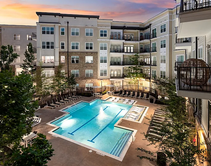 Chic apartment complex featuring a luxurious outdoor pool area with stylish lounge chairs, set against a backdrop of modern architecture at sunset.