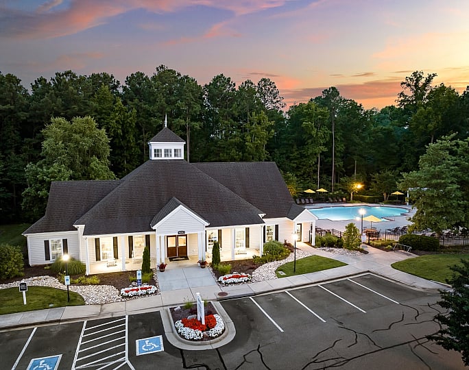 Charming clubhouse with inviting pool surrounded by lush greenery at sunset, perfect for relaxation and gatherings.