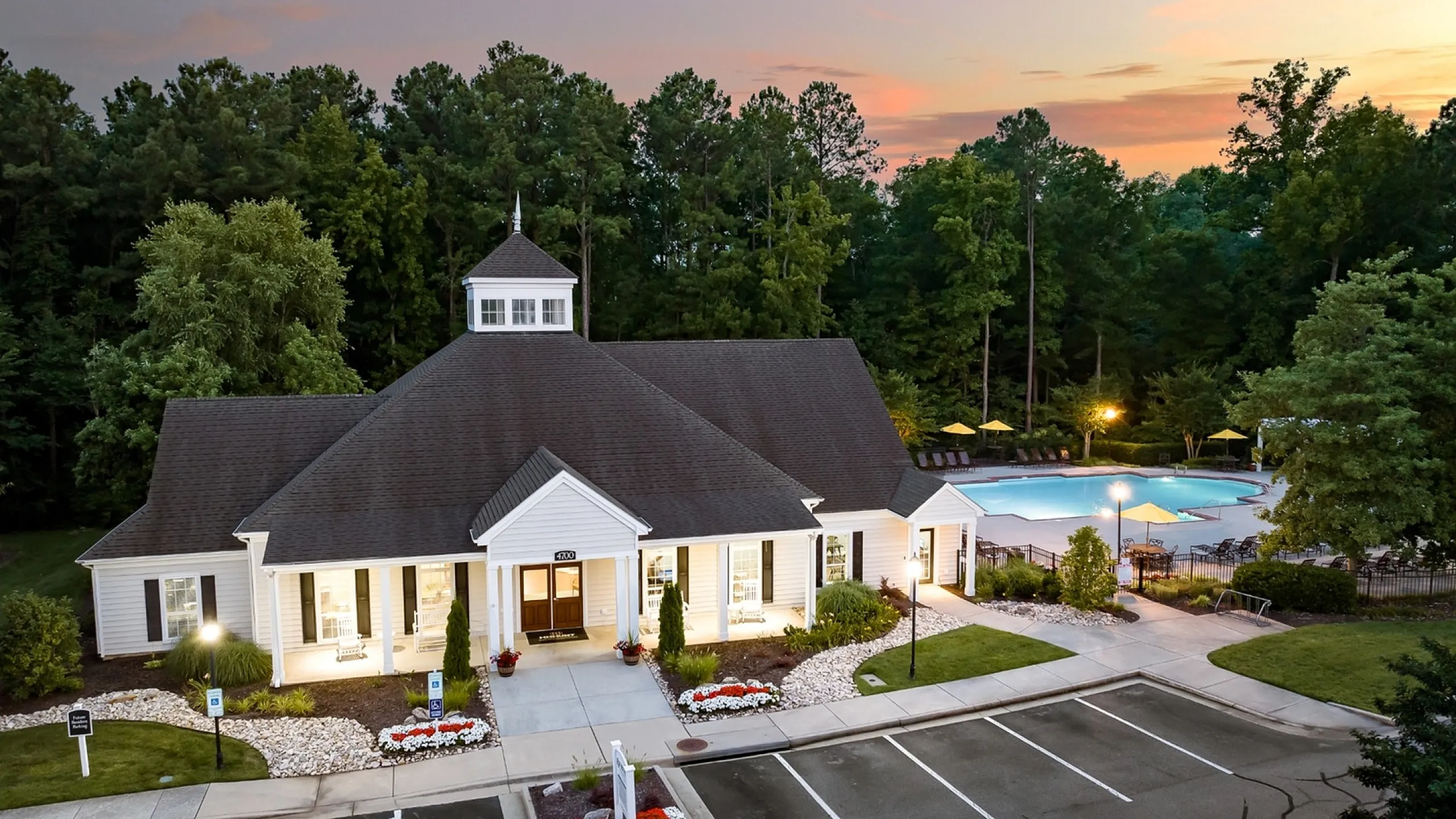 Charming community clubhouse surrounded by lush greenery, featuring a beautifully lit facade at sunset, with nearby luxurious pool area.