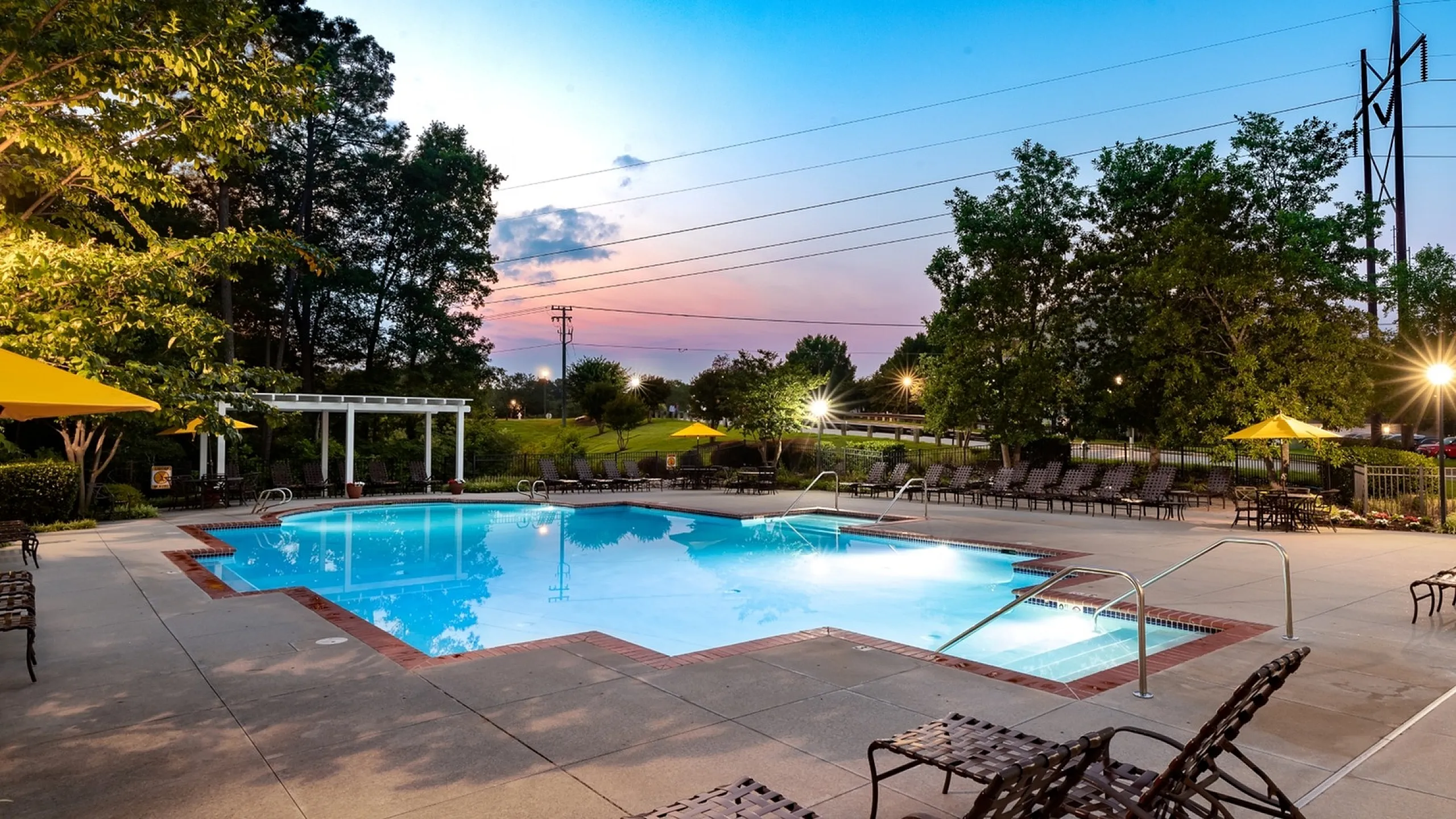 Tranquil outdoor swimming pool surrounded by lush greenery and stylish seating at sunset.