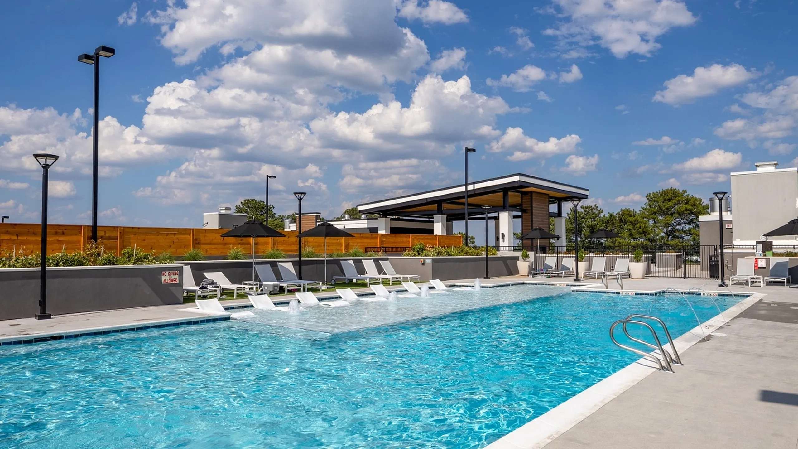 Luxurious outdoor swimming pool with elegant sun loungers, modern seating, and stylish umbrellas under a bright blue sky.