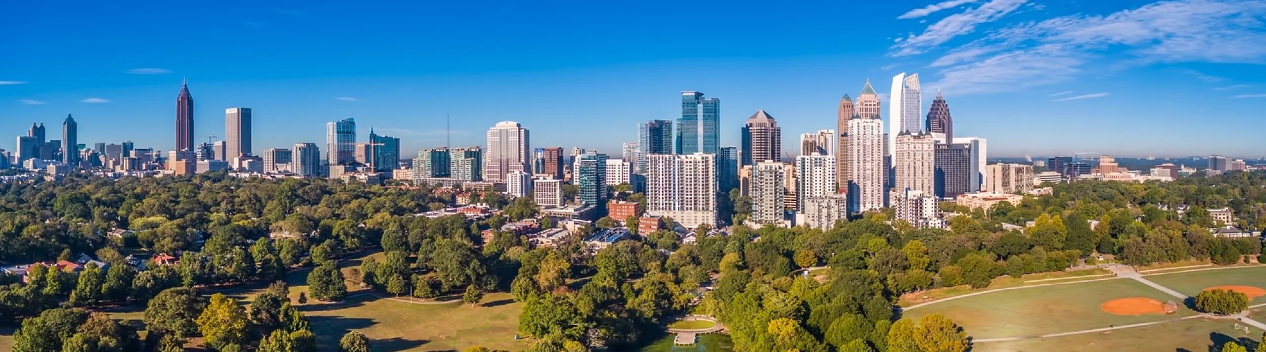 Breathtaking aerial view of a vibrant city skyline surrounded by lush green parks and a serene river on a sunny day.