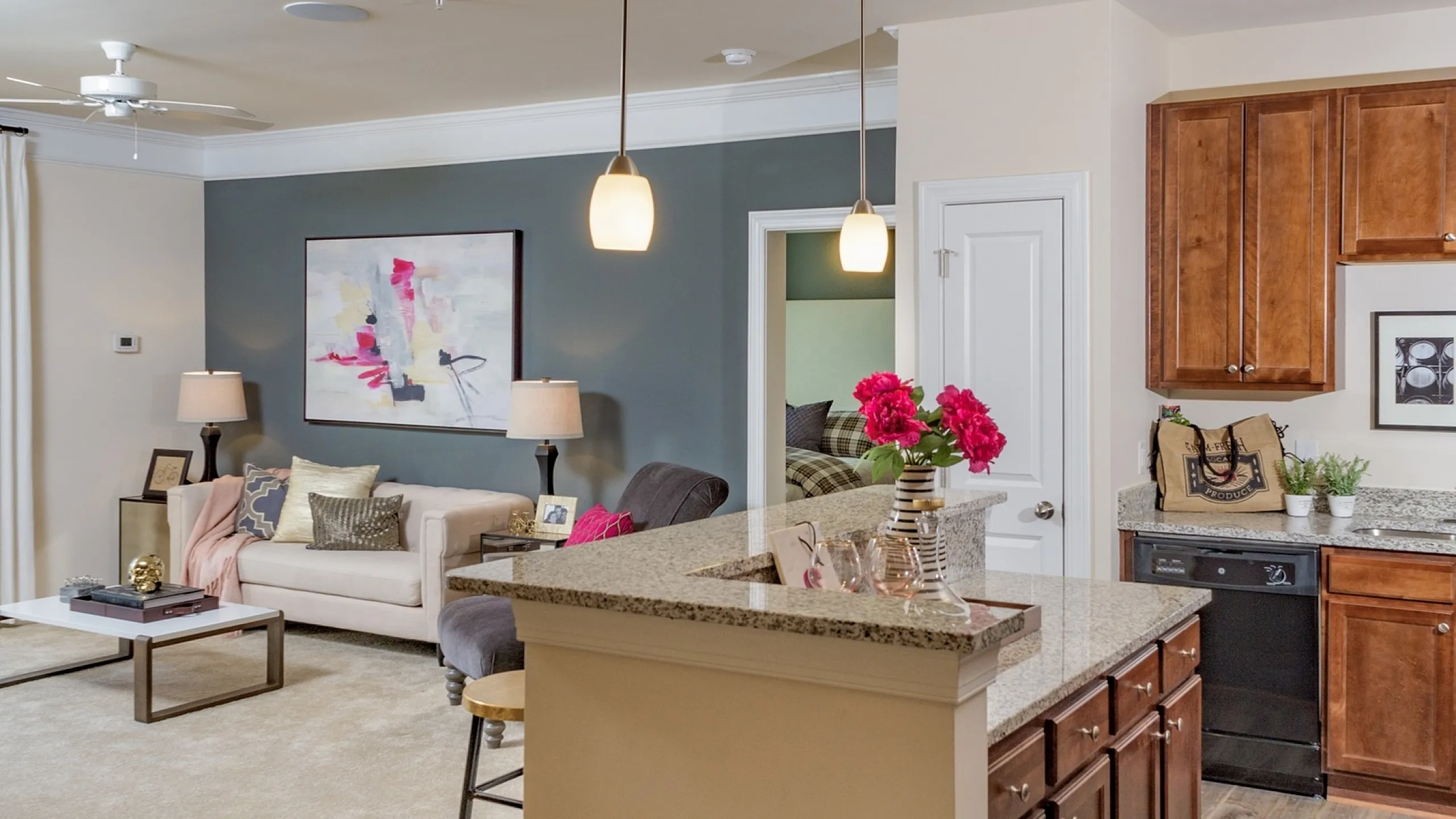Inviting open-concept living area showcasing a cozy sofa, modern art, and elegant pendant lighting, complemented by a stylish kitchen with granite countertops.