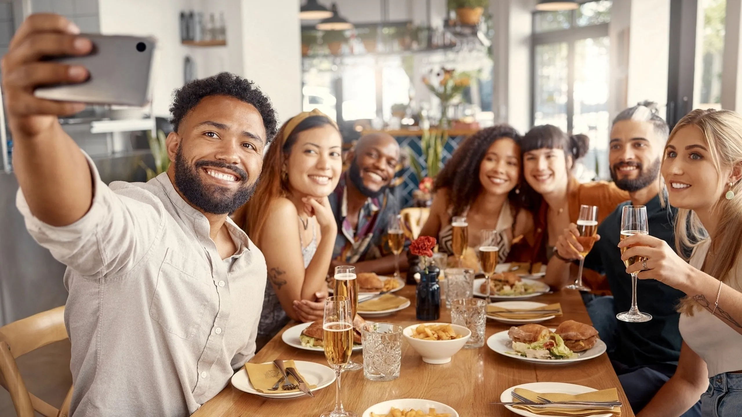 Joyful group of friends capturing a selfie during a cheerful brunch, with plates of delicious food and glasses of champagne enhancing the lively atmosphere.