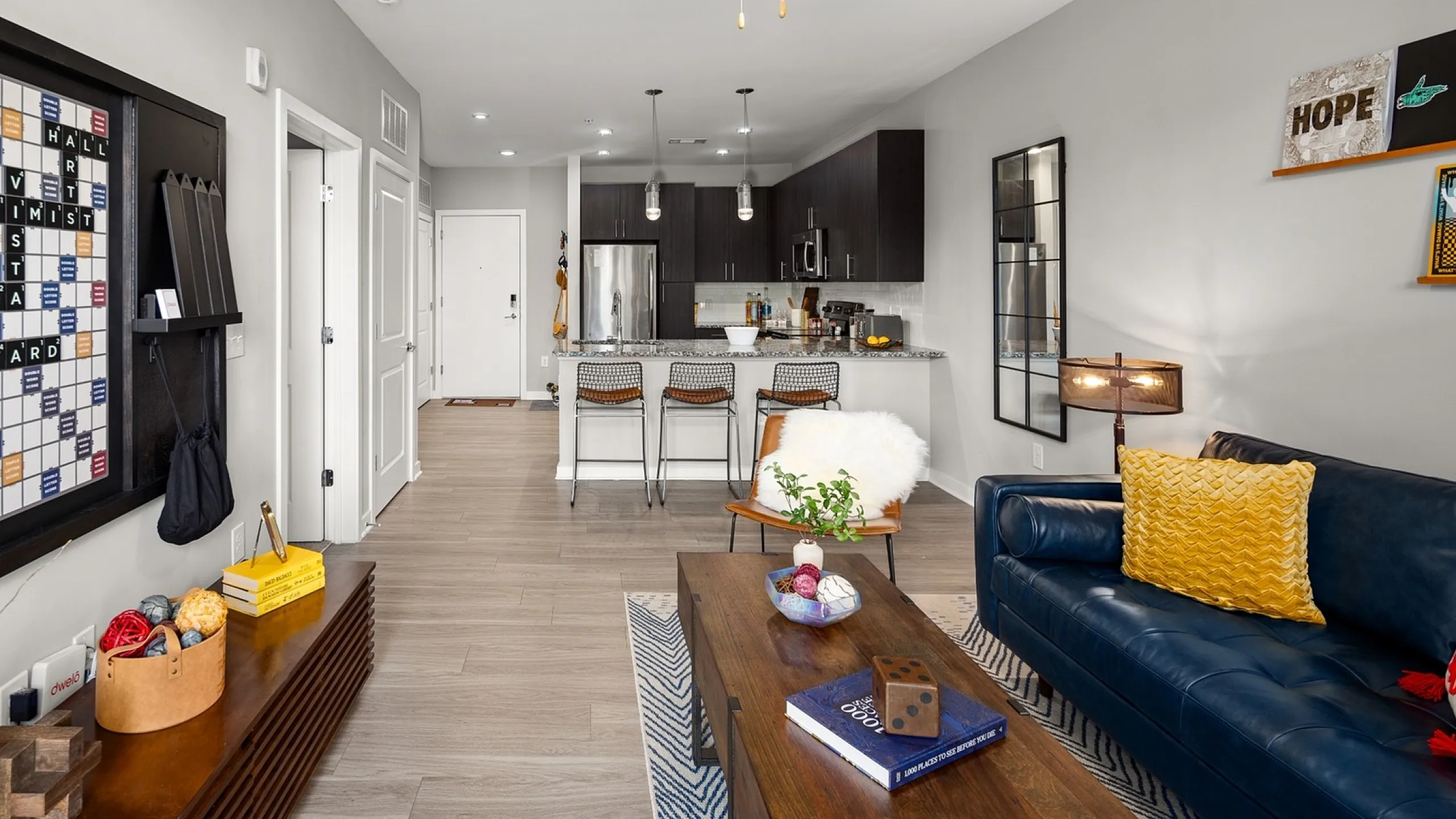 Modern open-concept living room with stylish decor, featuring a cozy blue sofa, sleek kitchen with bar seating, and vibrant accents.