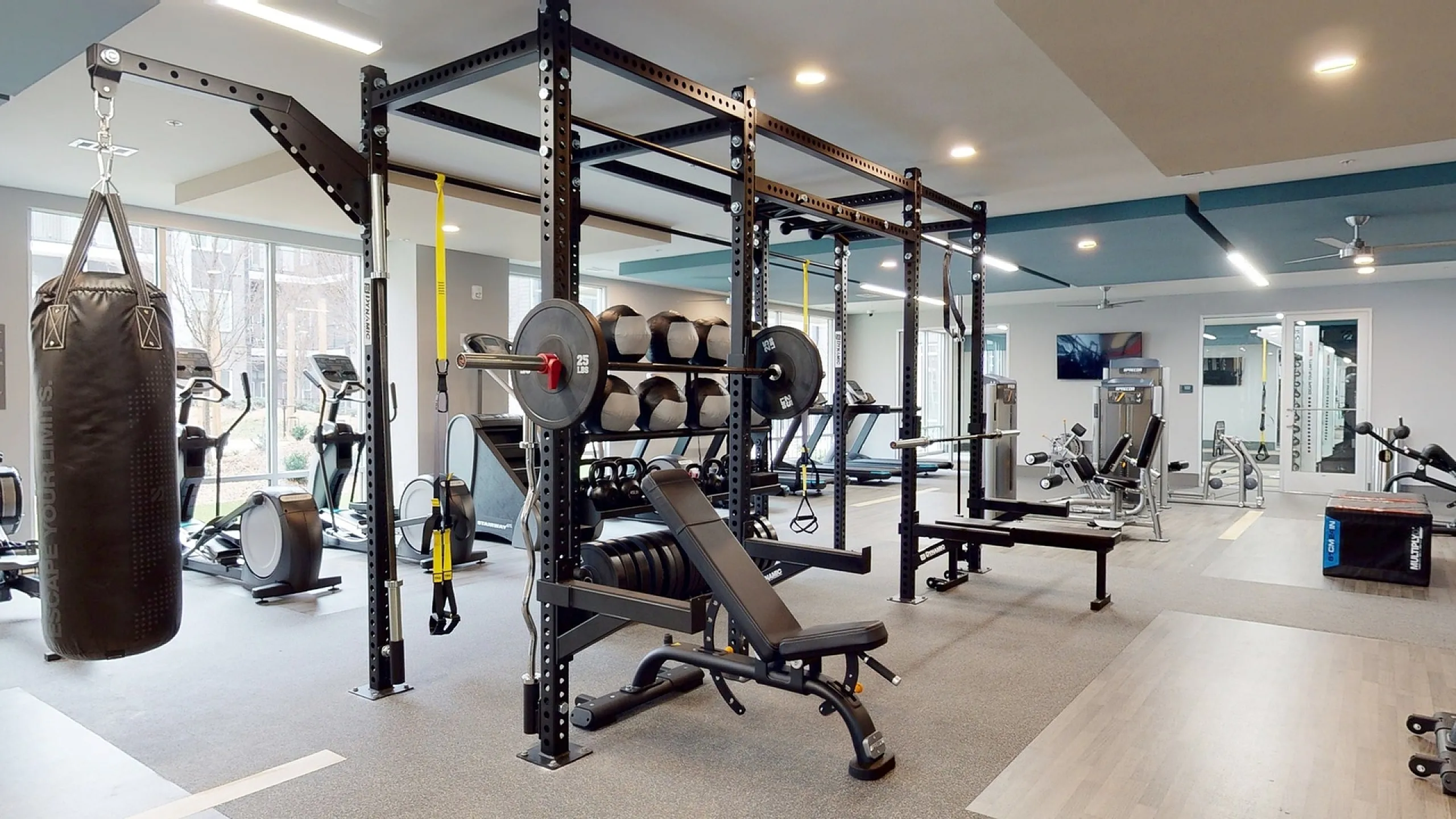 Modern gym with state-of-the-art equipment, featuring a boxing bag, weightlifting station, and cardio machines, perfect for fitness enthusiasts.