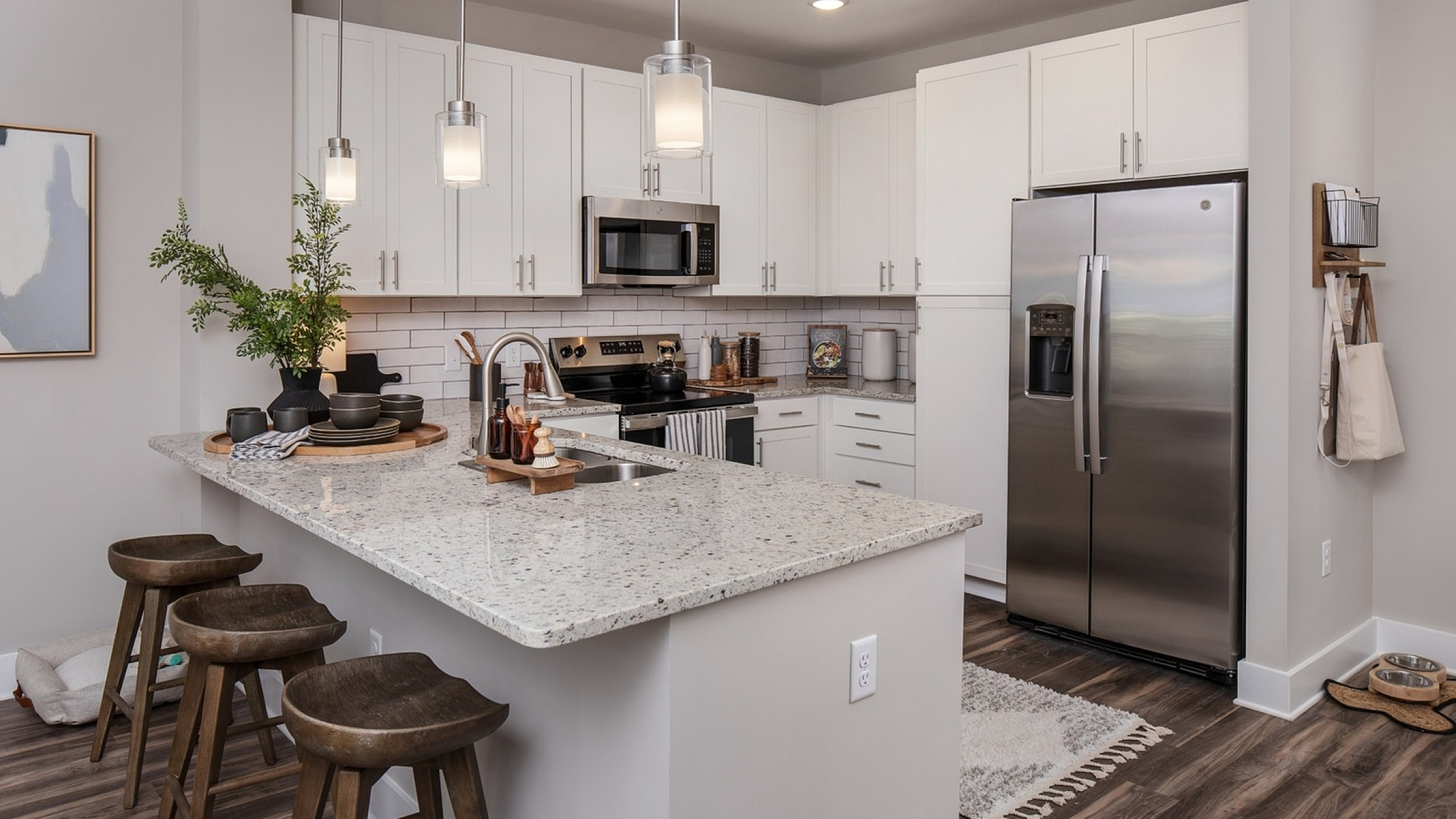 Modern kitchen with sleek white cabinetry, granite countertops, and stainless steel appliances, featuring elegant pendant lighting above a breakfast bar with wooden stools.