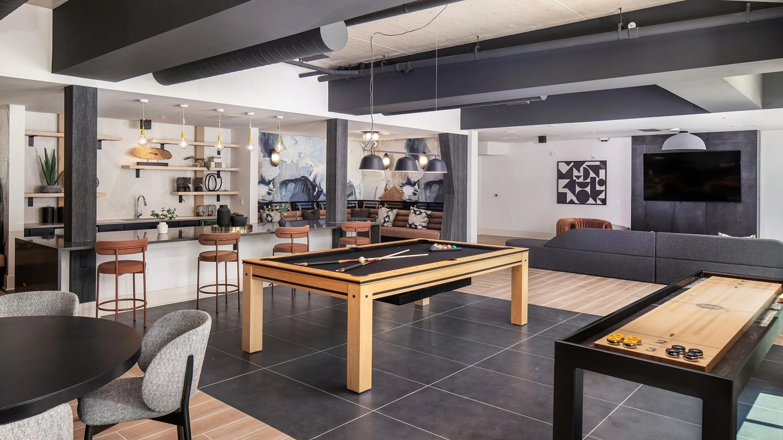 Chic apartment recreation area featuring a sleek billiards table, modern shuffleboard, stylish bar seating, and a cozy lounge with contemporary art.