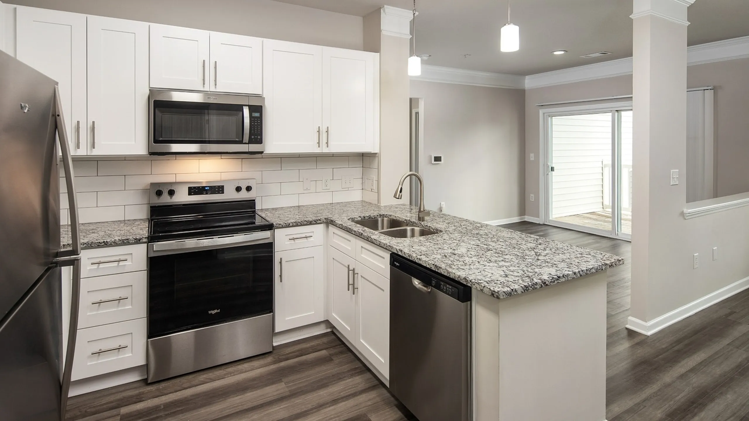 Modern kitchen with stainless steel appliances, elegant granite countertops, and chic white cabinetry leading to a spacious open-concept living area.