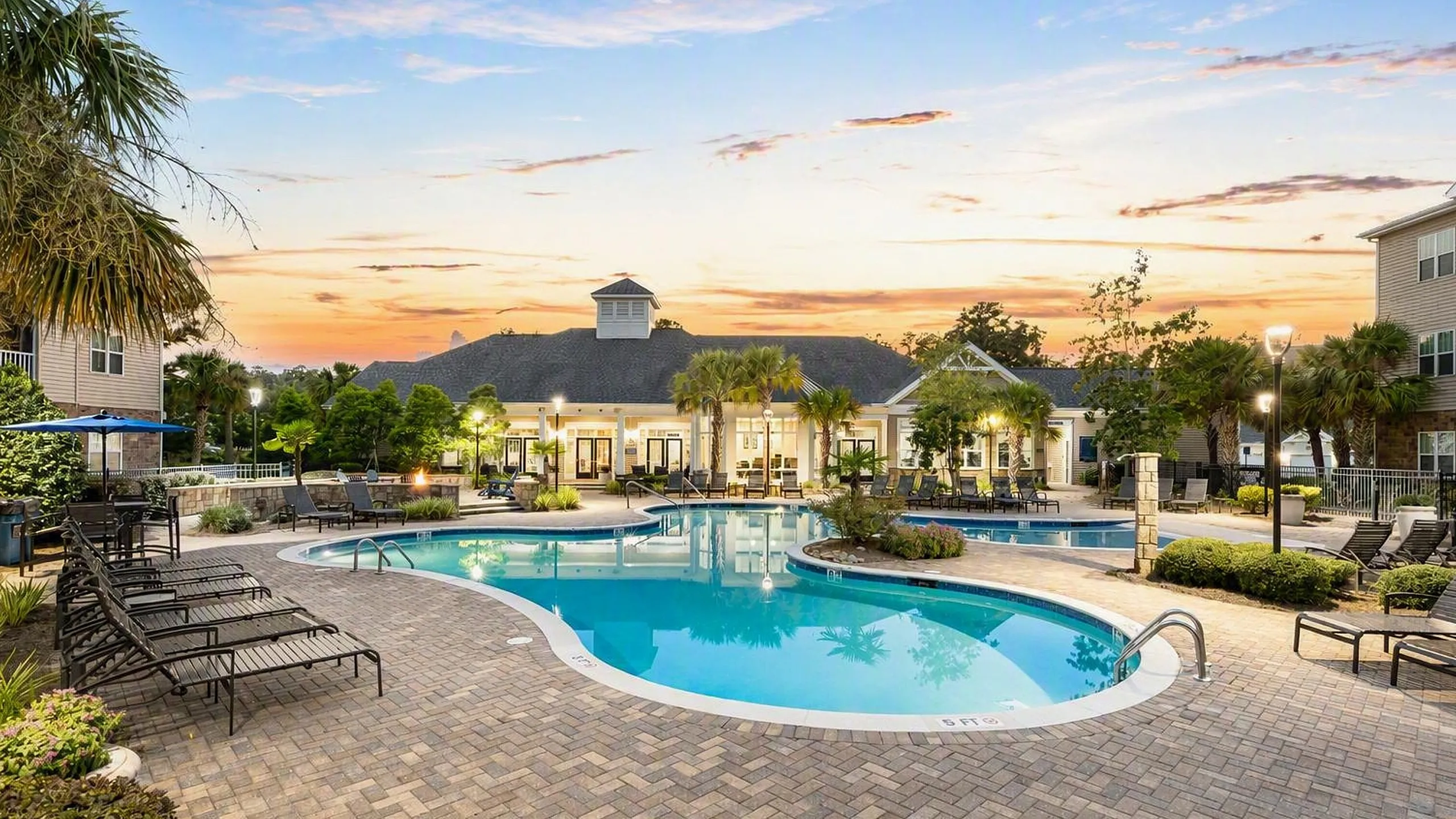 Resort-style pool area with luxury lounge chairs and lush landscaping at sunset, perfect for relaxation and social gatherings.