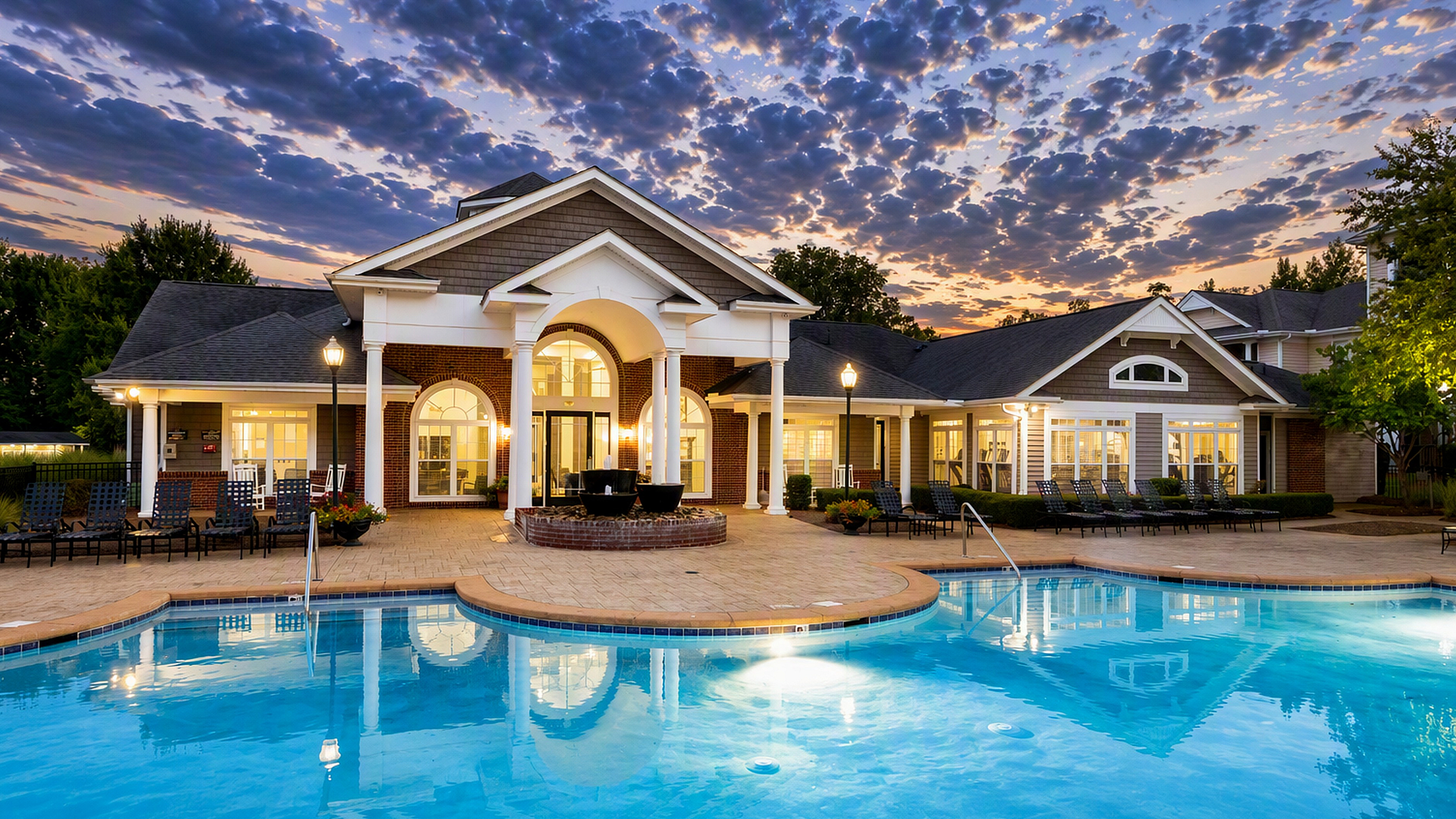 Elegant clubhouse with a large inviting pool and stunning sunset sky, perfect for relaxation and leisure.