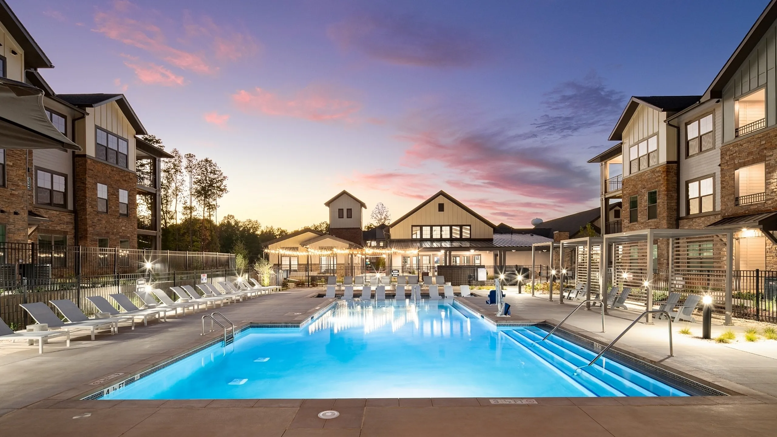 Luxury apartment complex featuring a beautifully illuminated outdoor pool area with lounge chairs and elegant lighting at dusk.