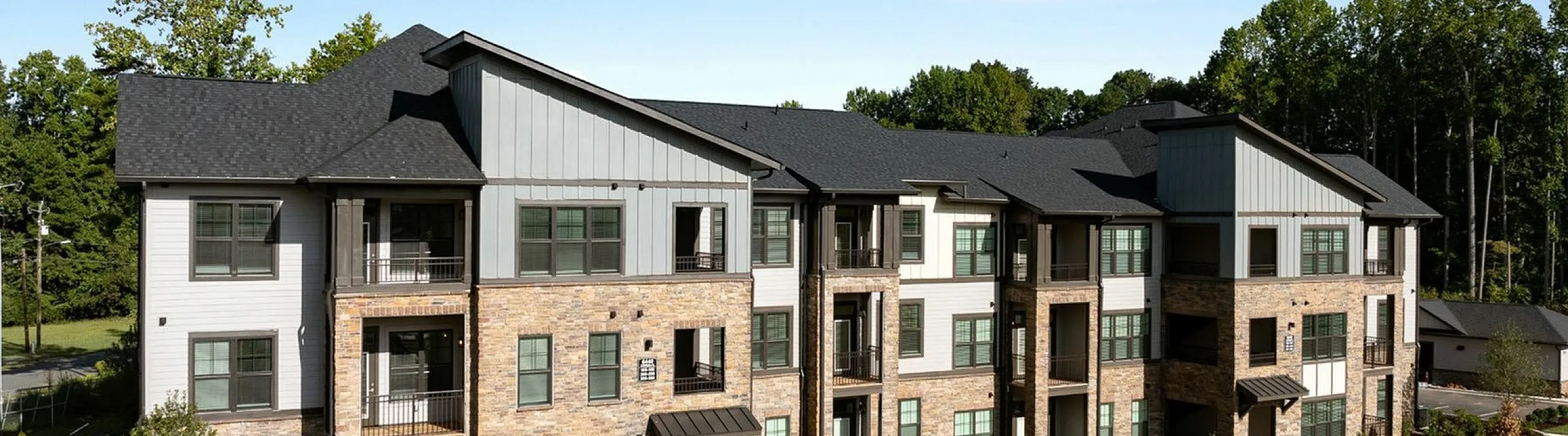 Charming modern apartment complex with beautiful stonework, surrounded by lush greenery and scenic views.