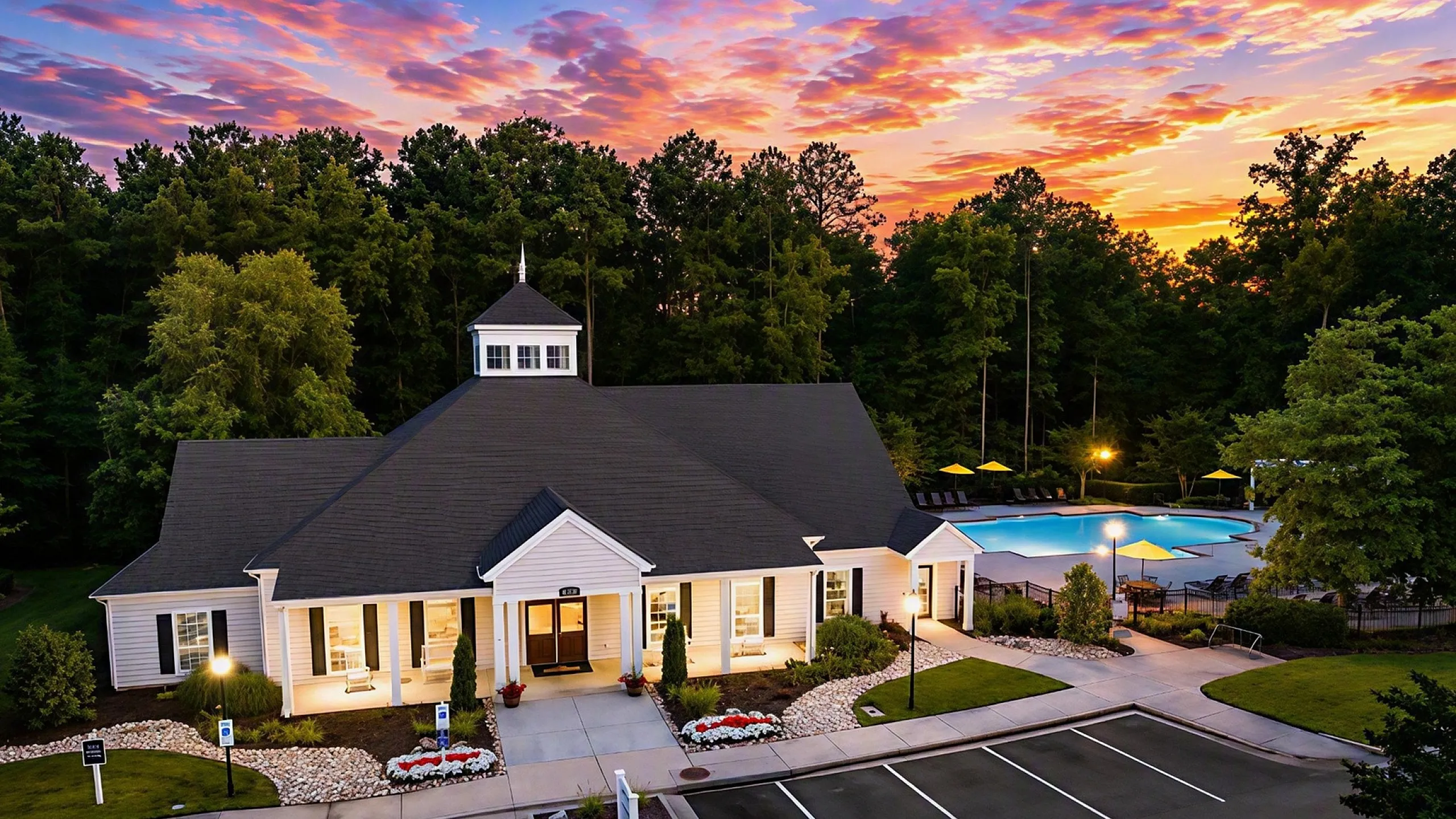 Charming residential clubhouse with elegant architecture, surrounded by lush greenery and an inviting pool at sunset.