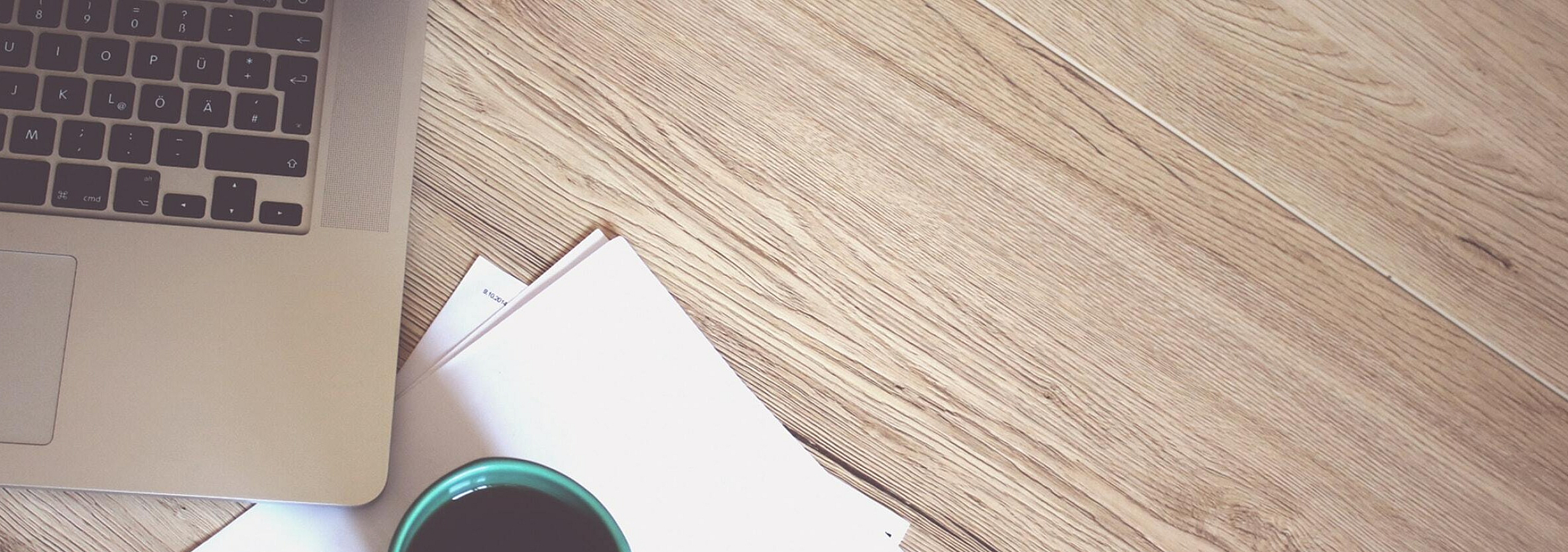 Cozy workspace setup with a sleek laptop, a stack of papers, and a steaming cup of coffee on a stylish wooden floor.